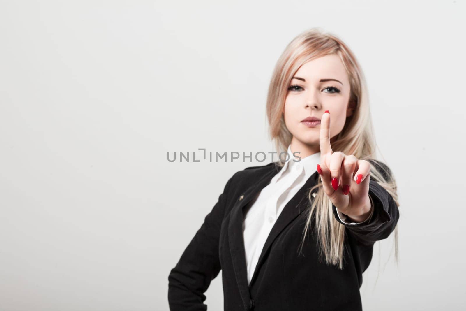 Confident businesswoman in white background, making stop gesture, exuding power and success. Elegant appearance, red nail polish, serious demeanor