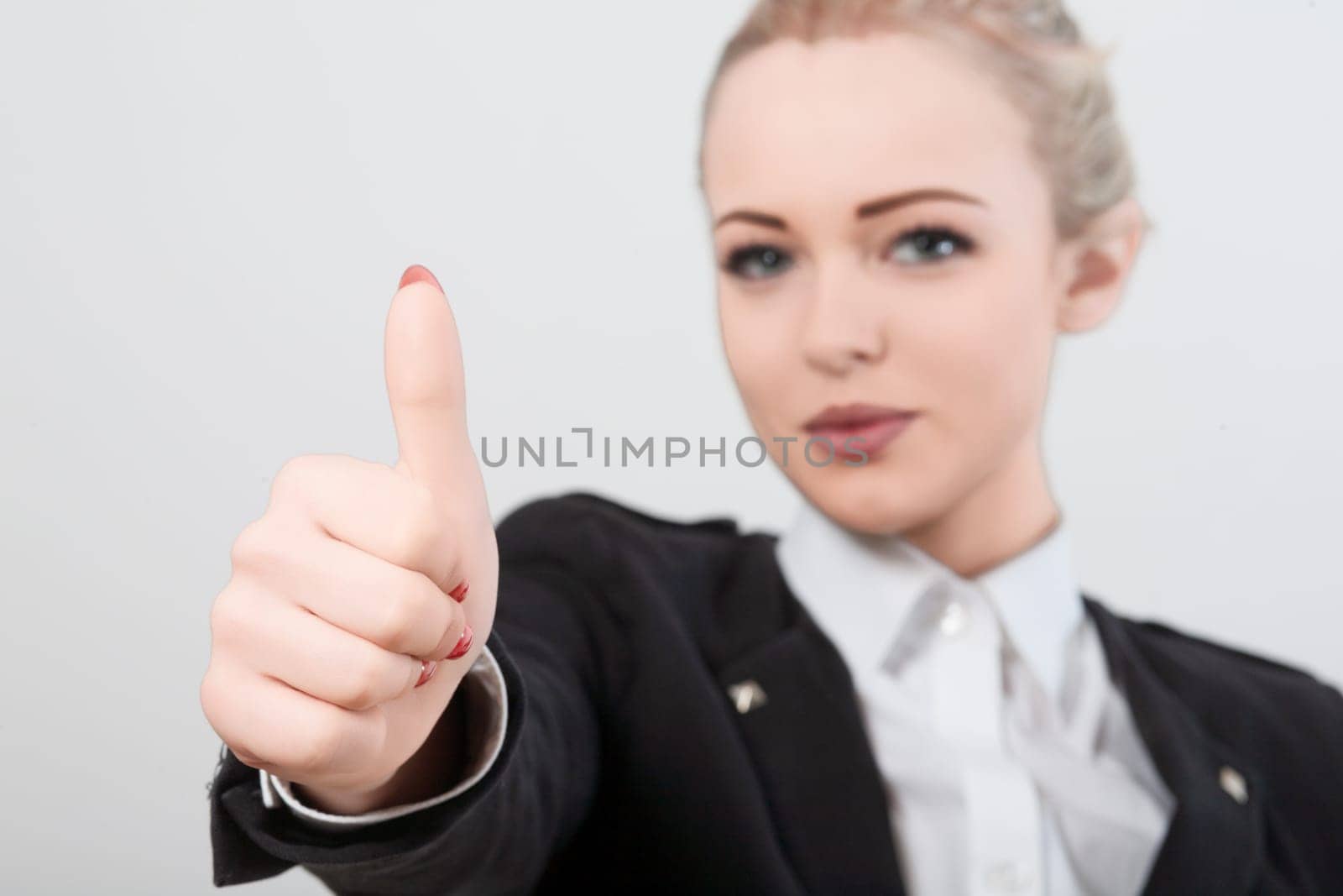 Confident businesswoman in black jacket and white shirt gives thumbs up against white background. Radiating positivity and success. Smile and body language show achievement and determination in career
