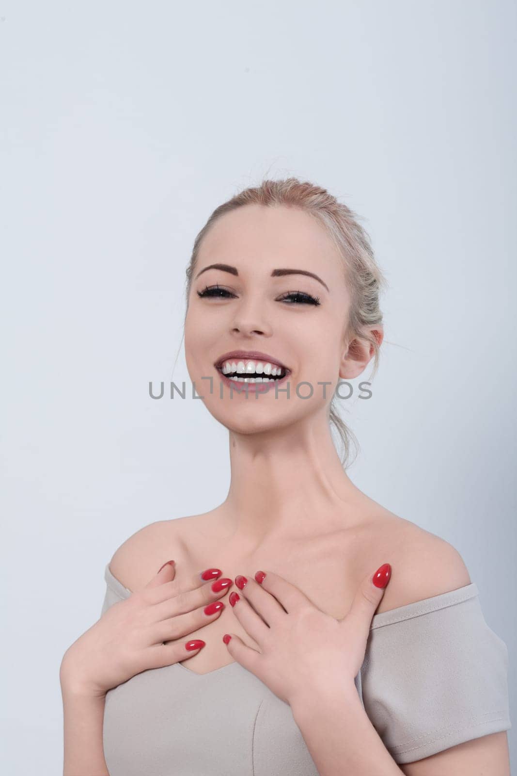 Attractive young woman with red nail polish is holding her hands to her chest and smiling broadly, expressing excitement and joy