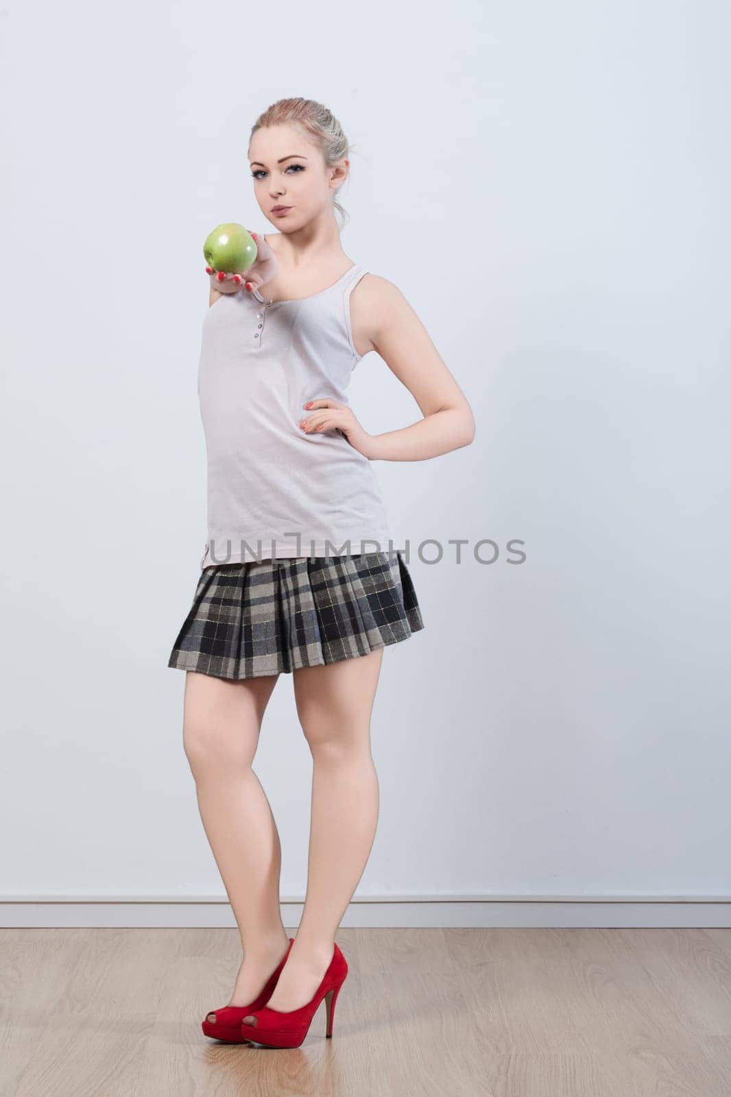 young woman, dressed in a plaid skirt and red heels, holds a green apple with a knowing expression. The apples metaphorical meaning suggests a playful nod to temptation and decision
