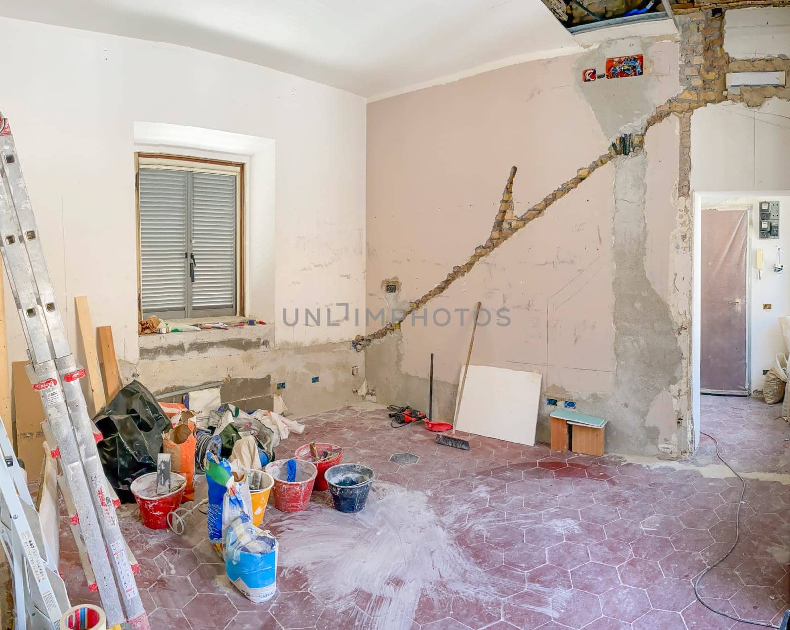 An unfinished room during a home renovation with construction tools, materials, and a ladder scattered around. Exposed brick and plaster walls under reconstruction