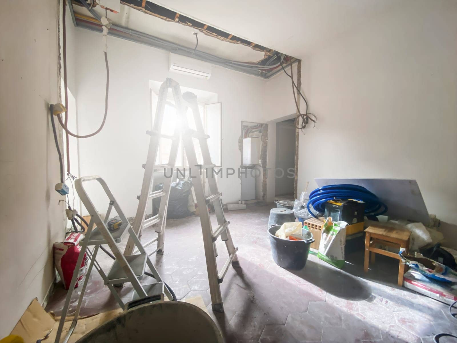 Interior of a room under renovation with exposed wiring, construction tools, debris, and damaged walls, showing ongoing reconstruction work.