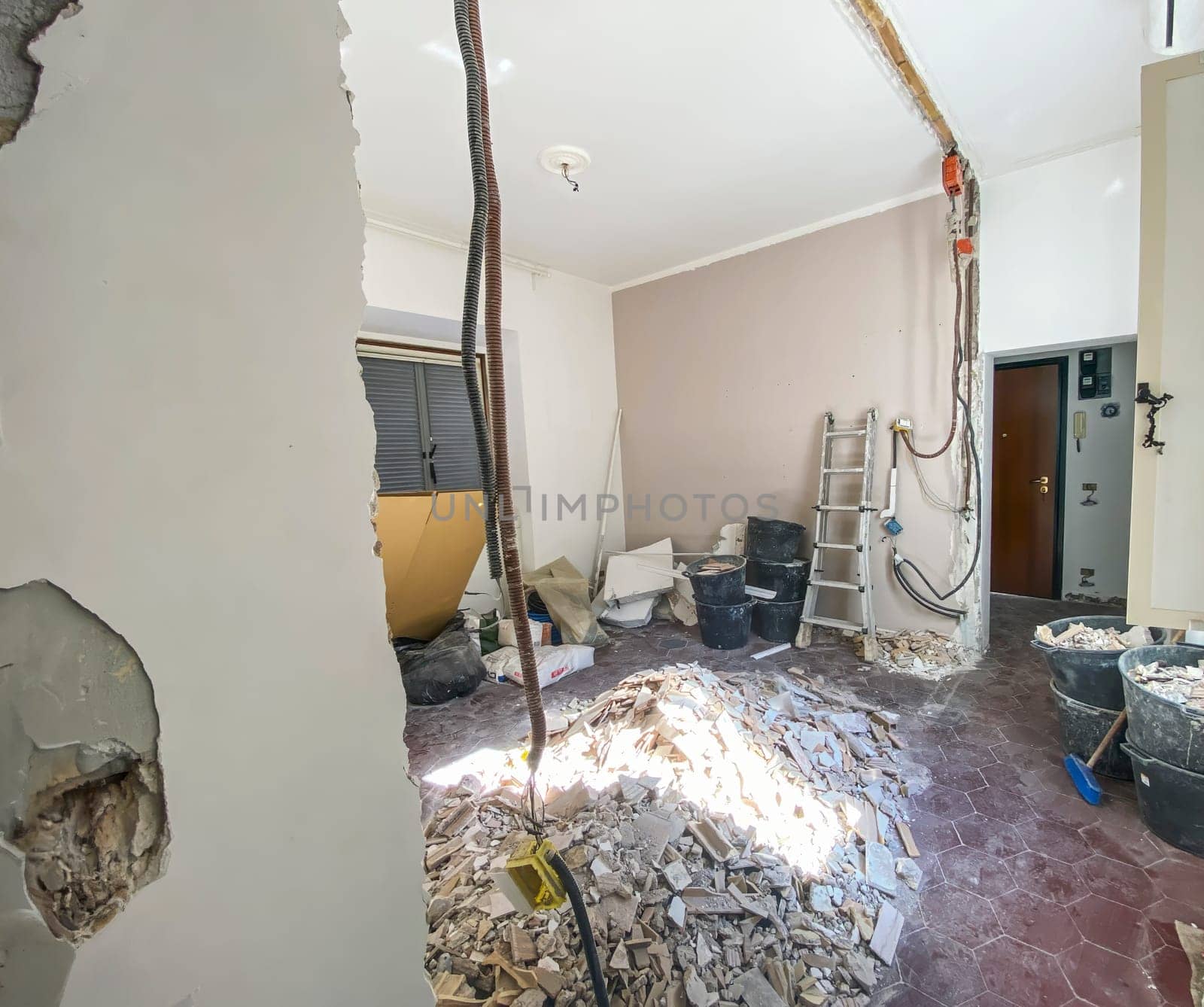 Interior of a room under renovation with exposed wiring, construction tools, debris, and damaged walls, showing ongoing reconstruction work