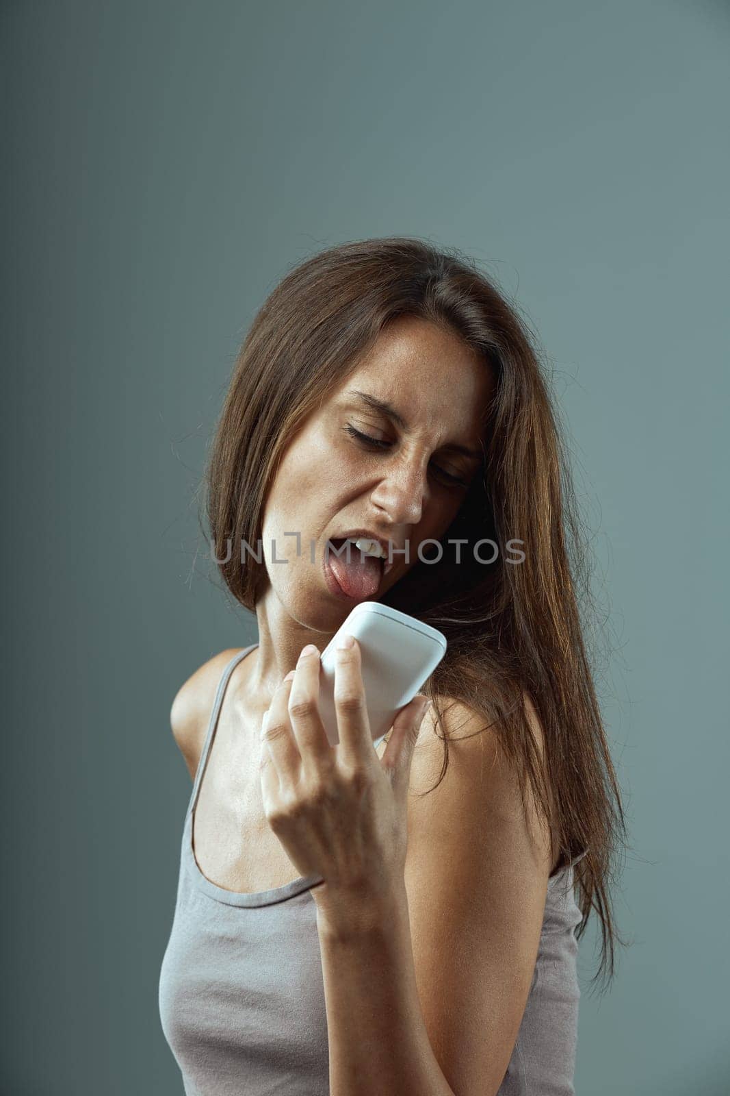 Woman is holding a smartphone close to her face and sticking out her tongue, expressing a sense of disgust or frustration with technology