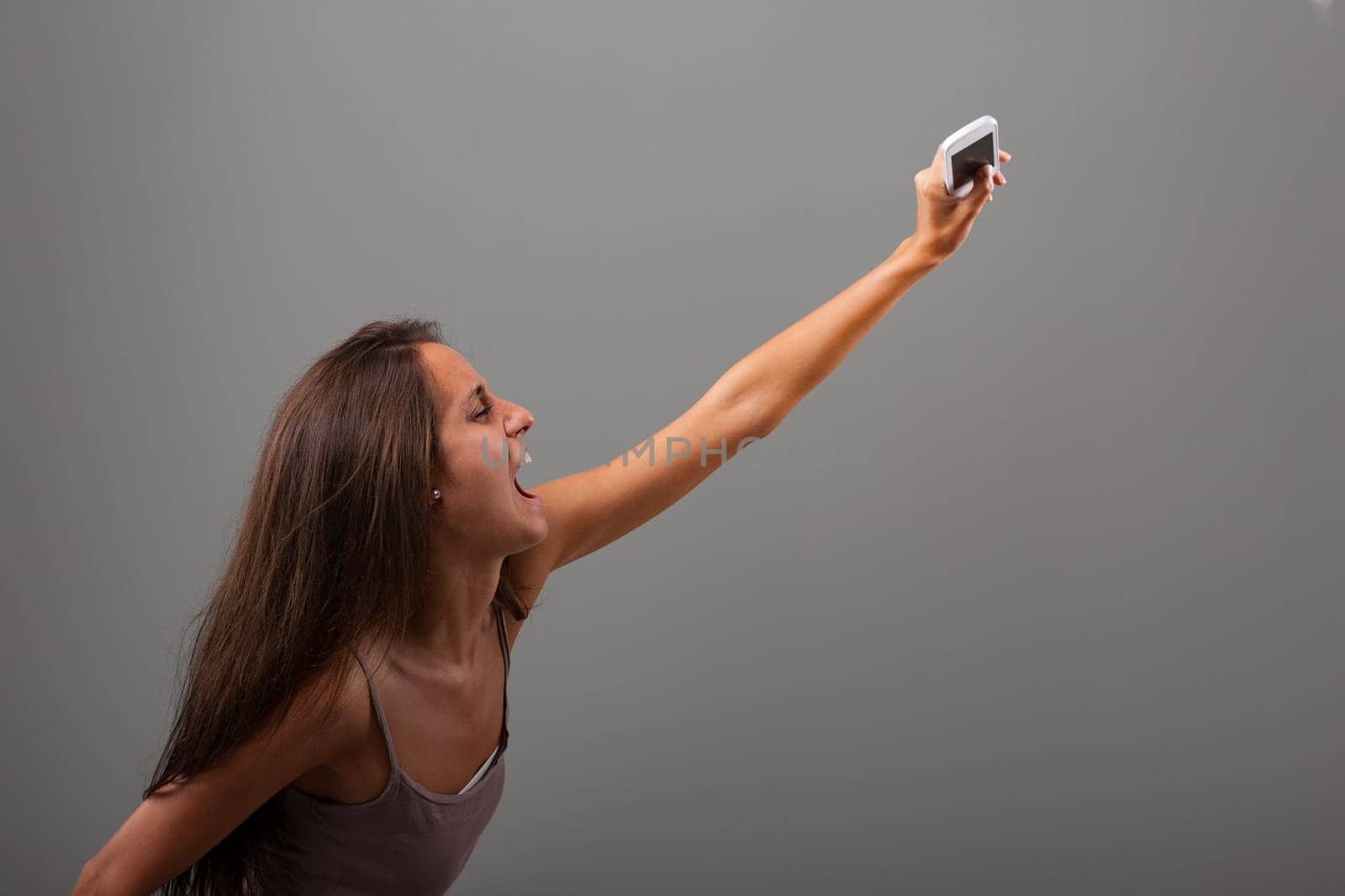 Young woman is screaming while holding a smartphone with an outstretched arm, expressing a mix of frustration and excitement