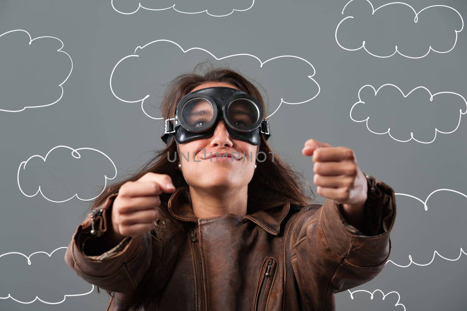Confident young woman pretends to fly a plane through fluffy clouds, embodying freedom and adventure with a joyful smile and determined gaze