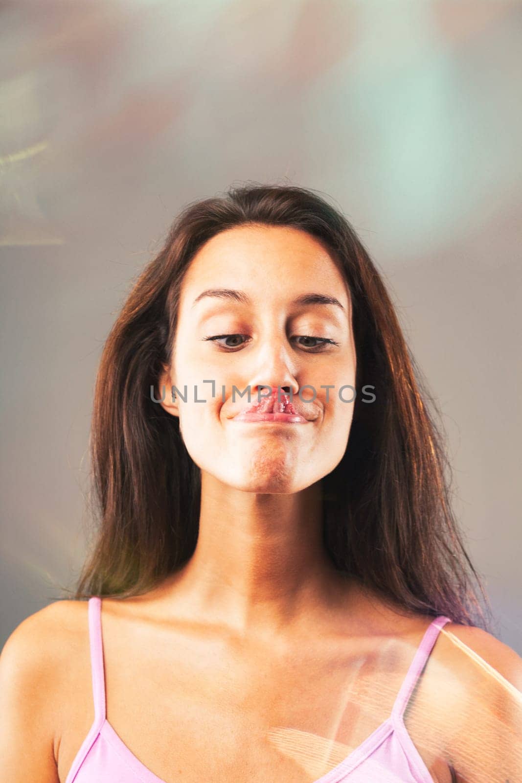 Young woman playfully sticks out her tongue and makes a funny face, exuding joy in a pink top with long brown hair