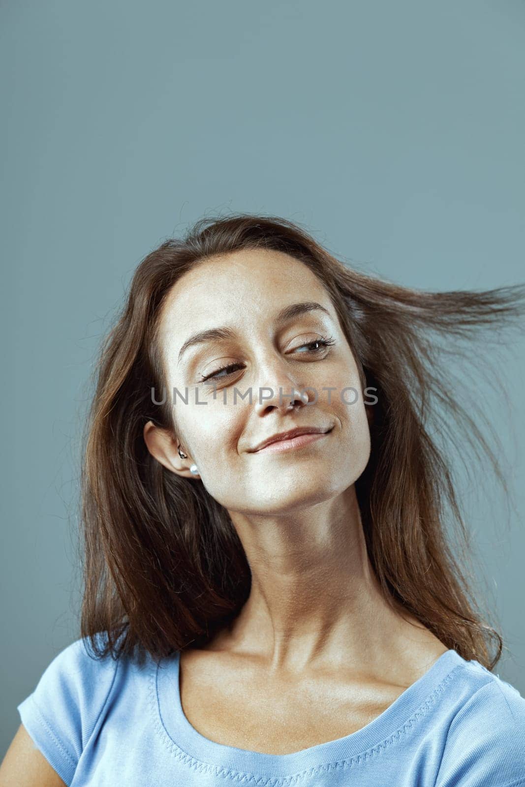 Young woman with long brown hair is flipping her hair and smiling, conveying a sense of happiness and carefree attitude
