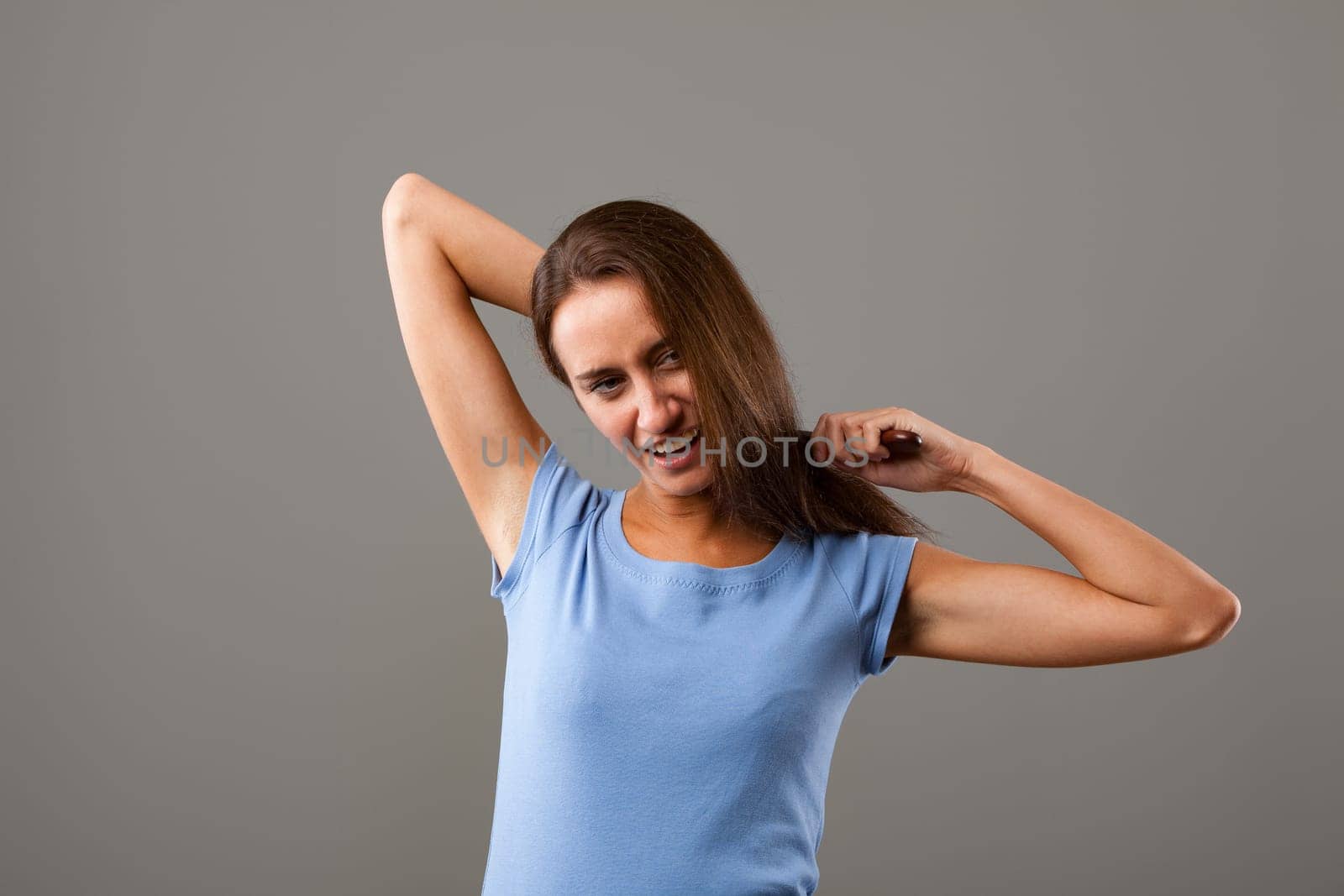 Frustrated young woman pulls at her long brown hair, showing anger, stress, and worry against a gray background