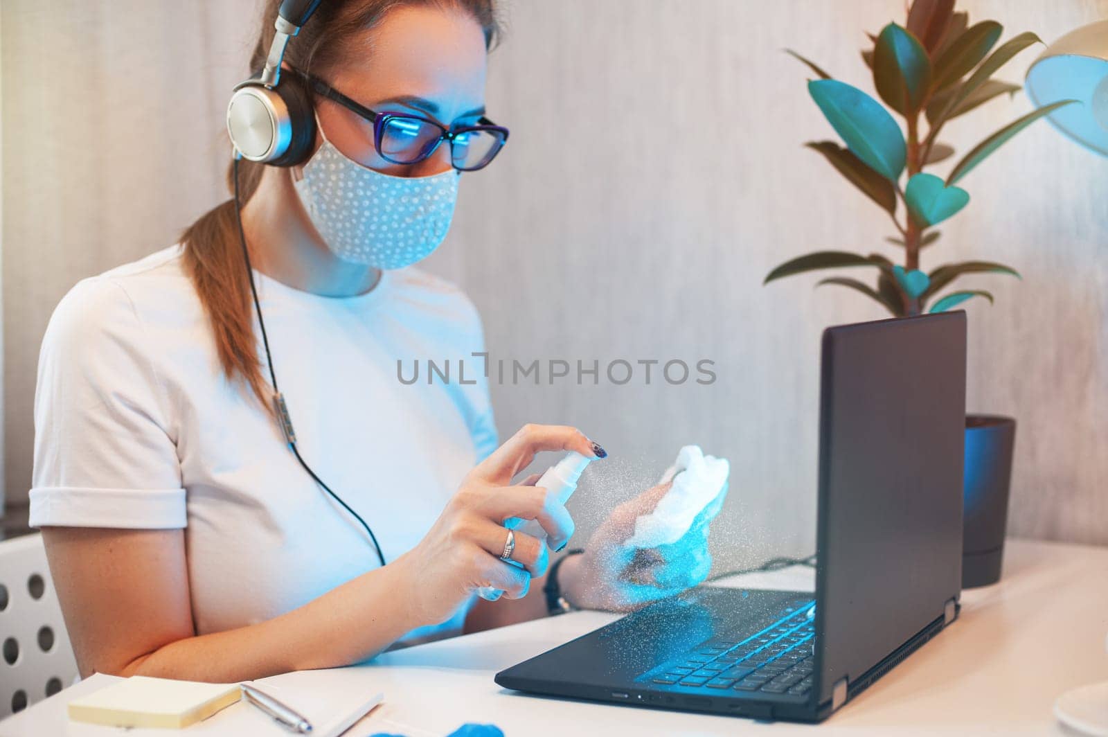 Woman disinfects the surface of the phone by sanitizer spray on the working place. Coronavirus concept. Woman in quarantine for coronavirus covid-19 working from home.