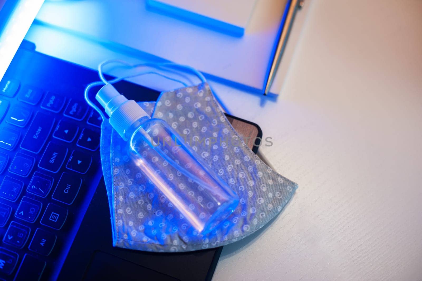 Sanitizer anti virus spray and protective mask on the working table with laptop. Personal hygiene concept. Concept of quarantine for coronavirus and working from home.