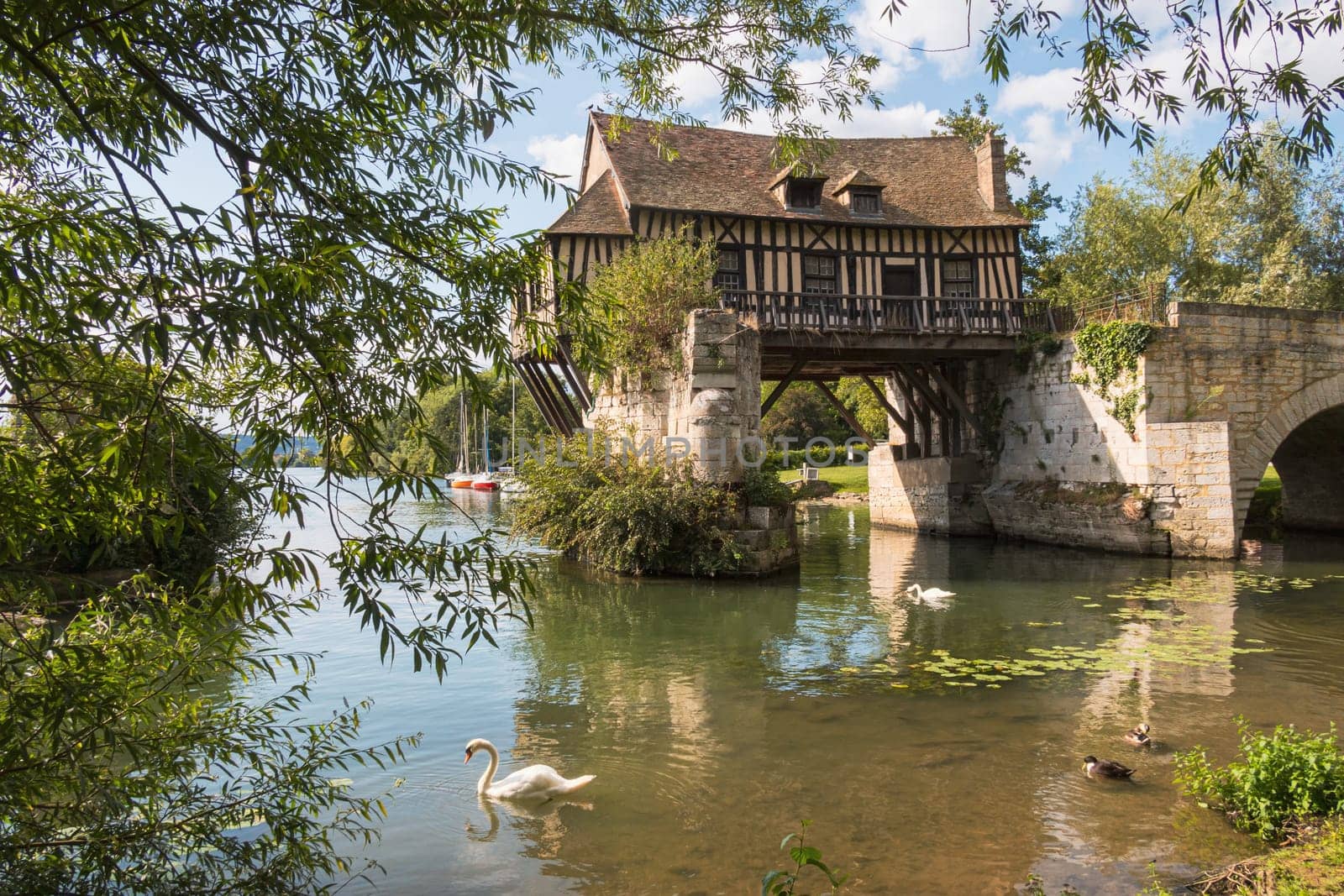The beautiful old mill on the broken bridge over the Seine river with swans in the foreground in Vernon, Normandy, France