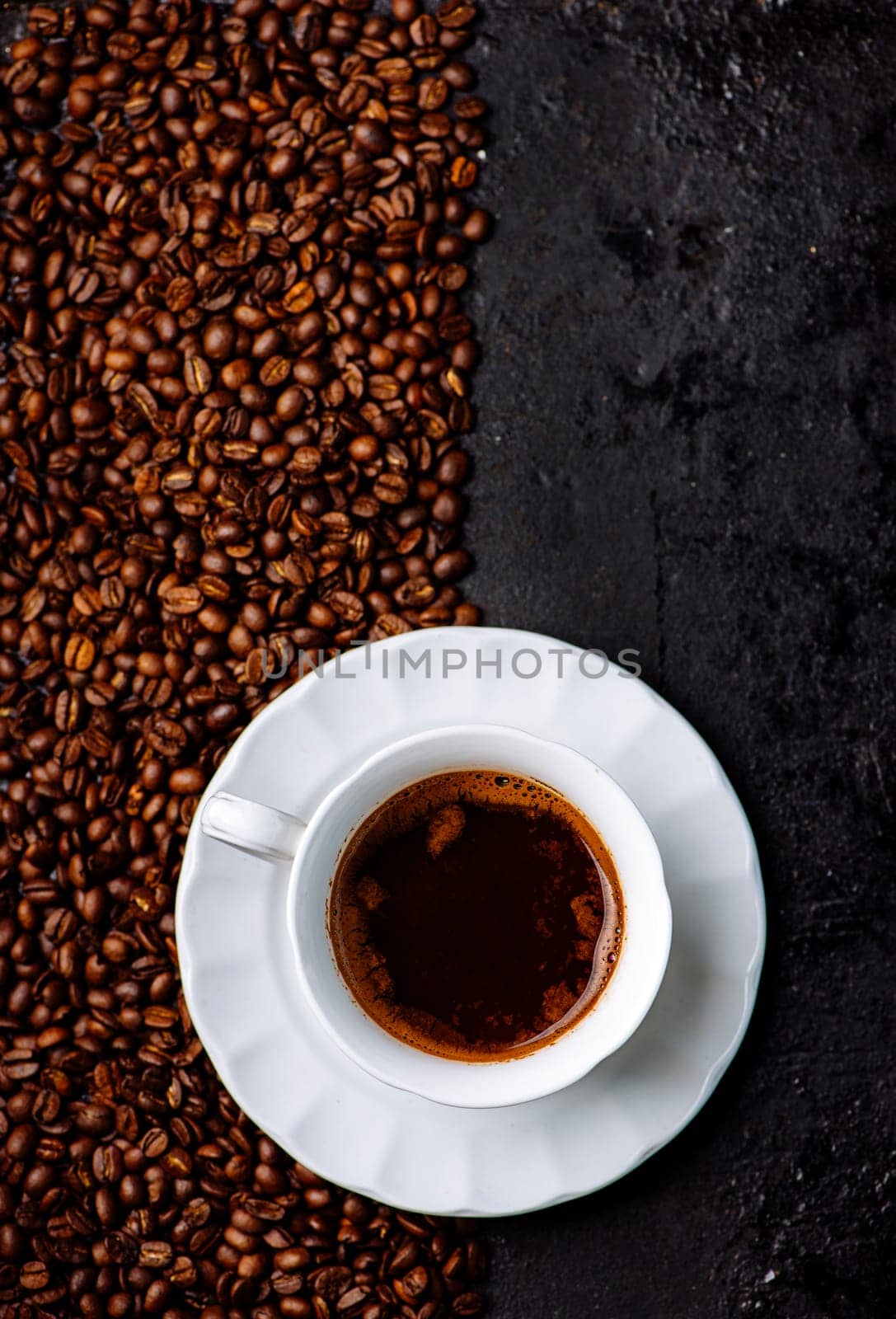 Top view of coffee cup on coffee bean texture and black rustic background. Hot beverage on vintage dark table. Minimal art design layout. Restaurant cafe shop creative menu.