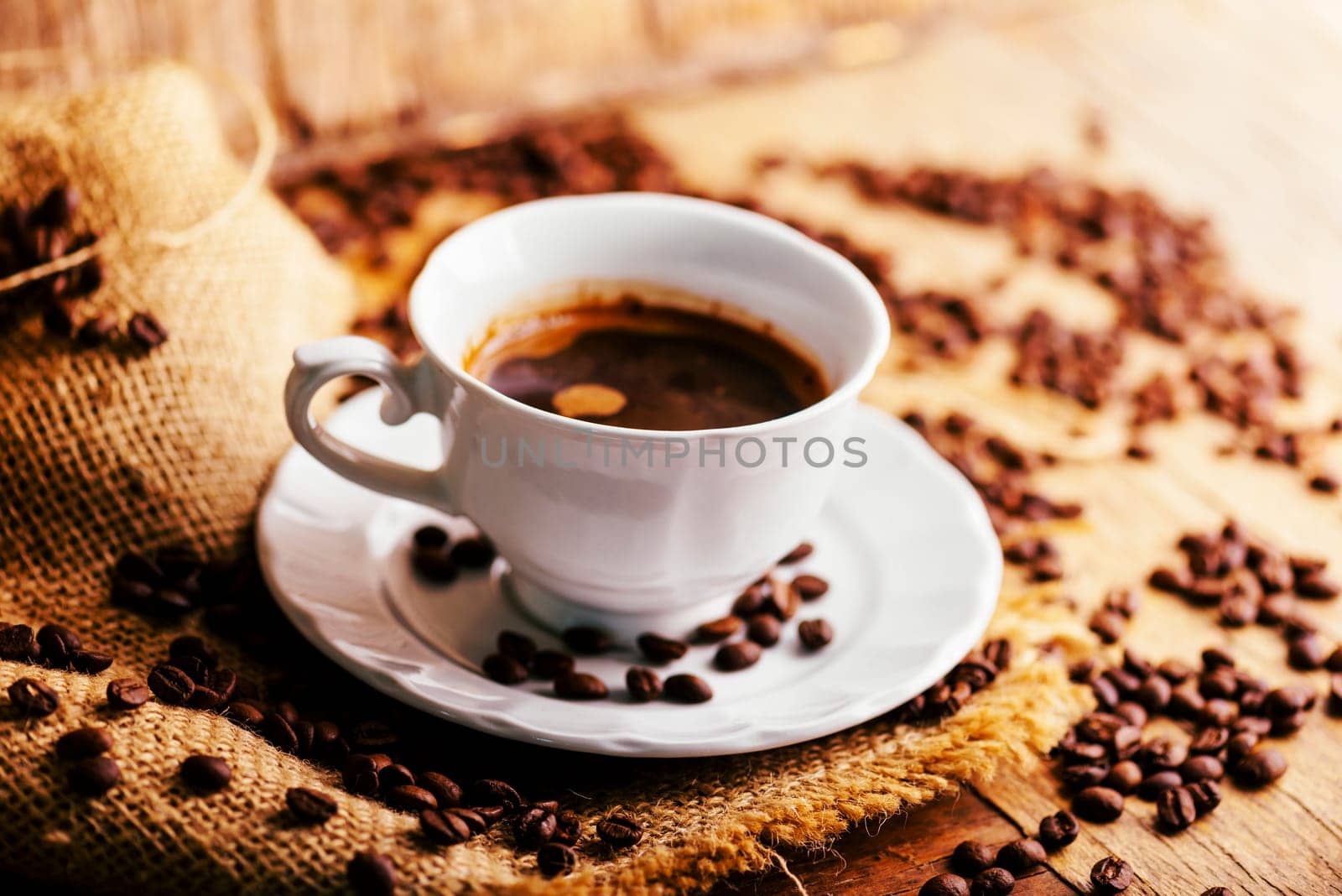 Closeup of coffee cup and coffee beans with vintage burlap on rustic wooden table. Hot beverage in mug still life. Cafe restaurant shop creative menu background.