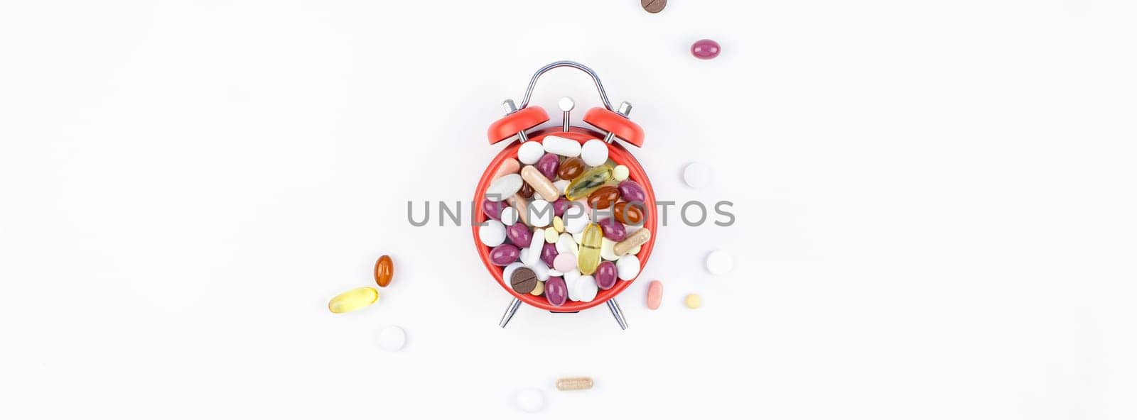 Nutritional supplement color pills on red alarm clock face isolated on white background with copy space. Template for feminine beauty blog social media. Female healthcare concept
