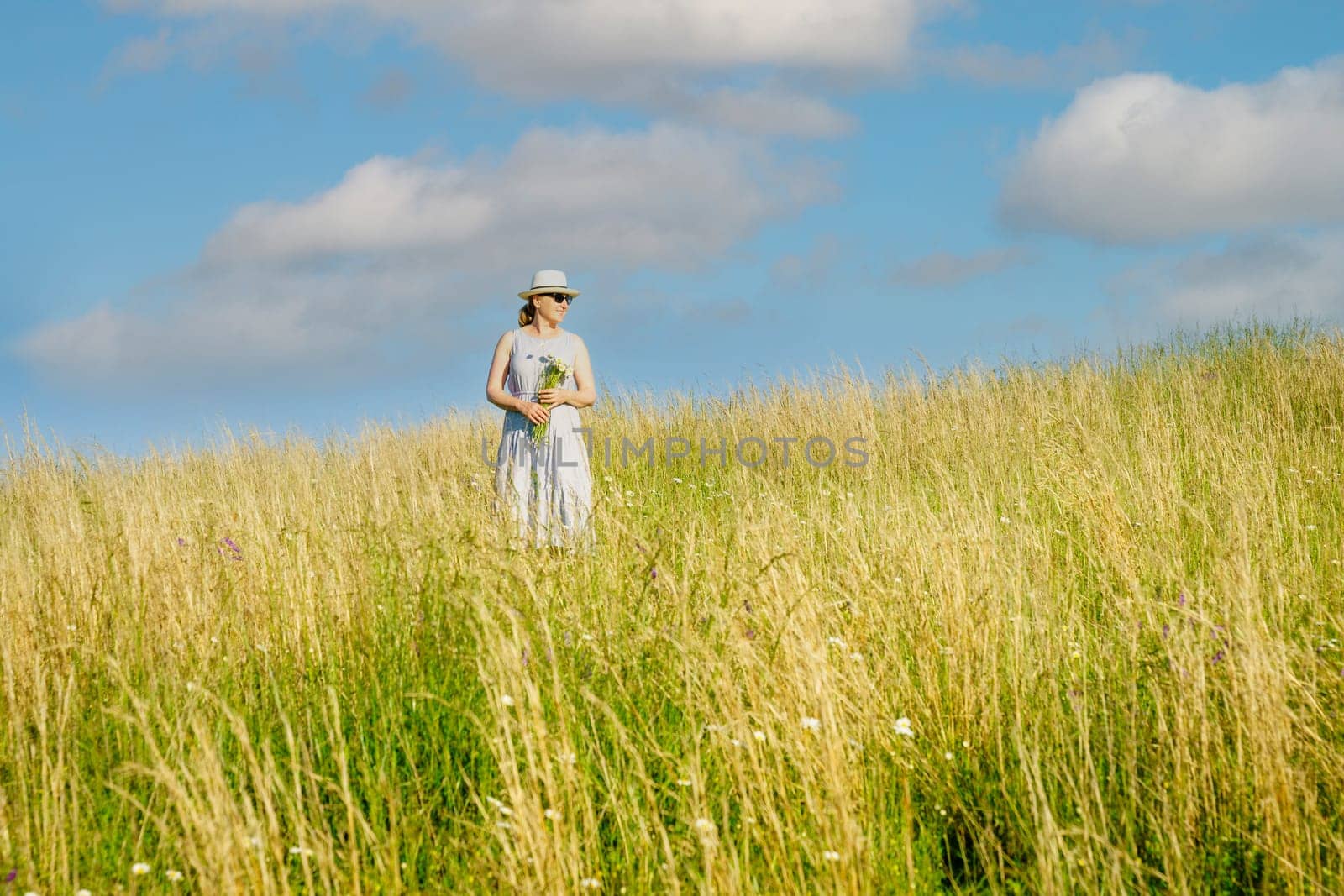 Happy mature woman with wildflowers in a tall grass field on a bright summer day.