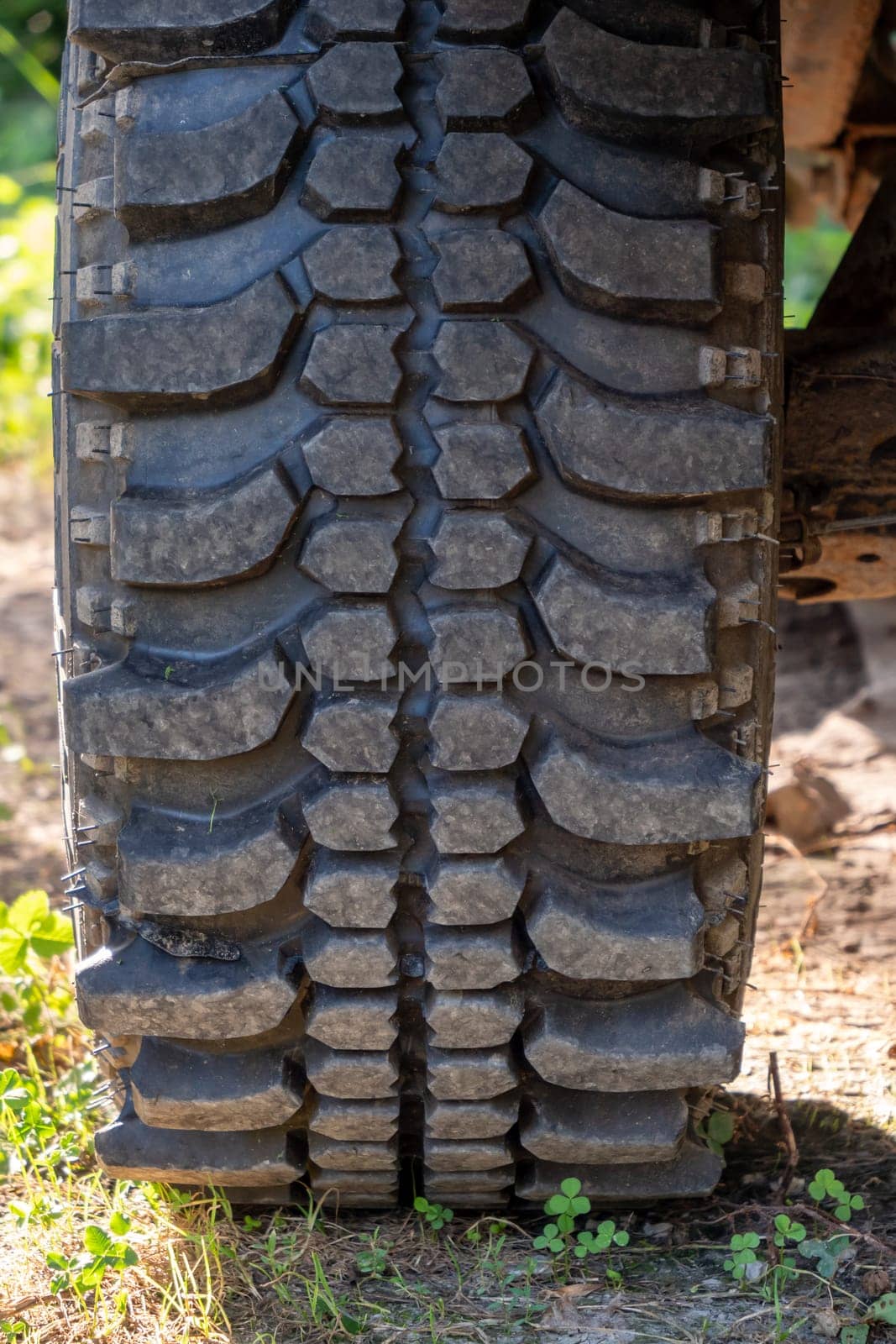A close up of a tire with a black tread. The tire is on a dirt road