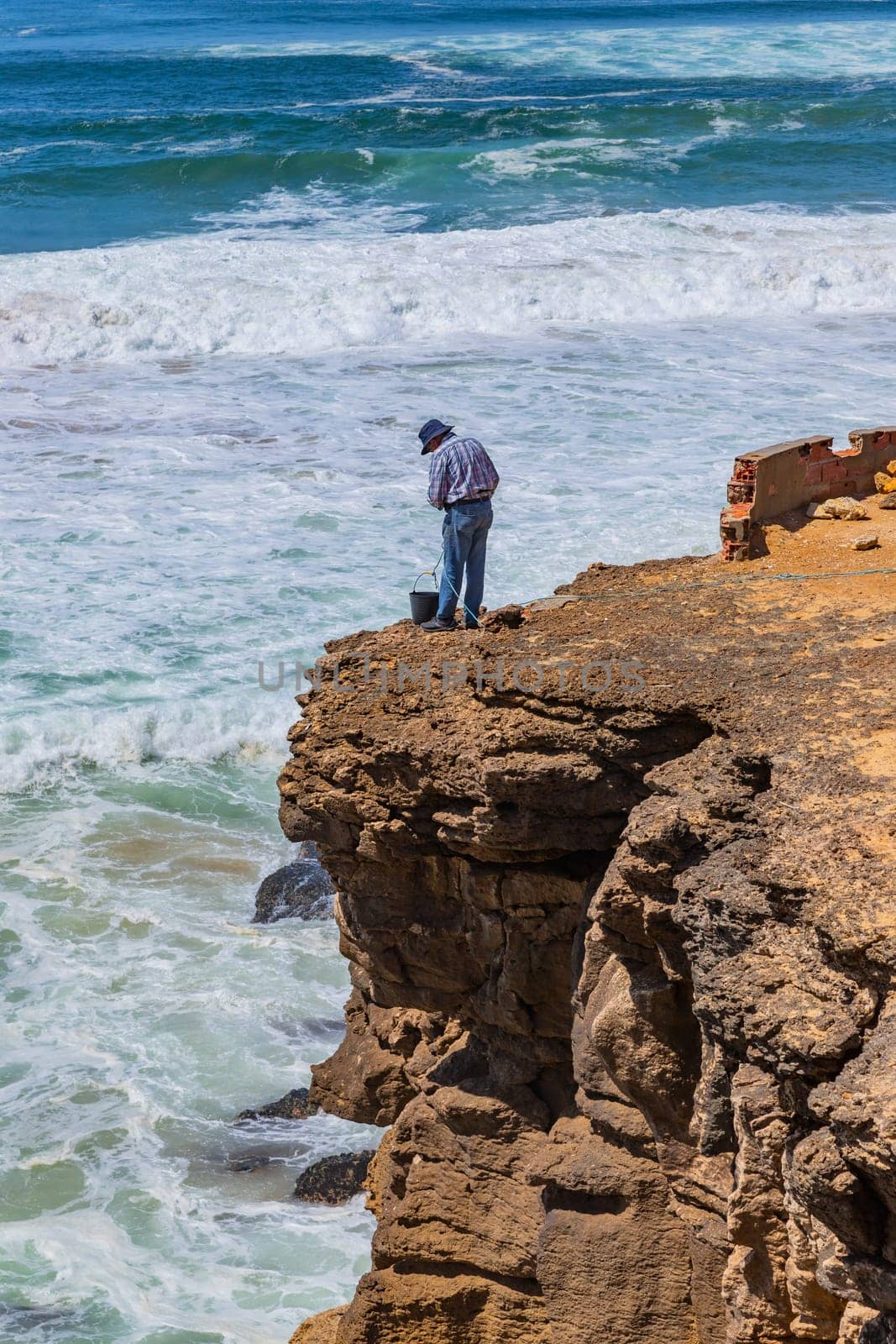Sintra, Portugal: April 13, 2024: A fisherman stands on the edge of a cliff by the ocean in Ericeira, Portugal