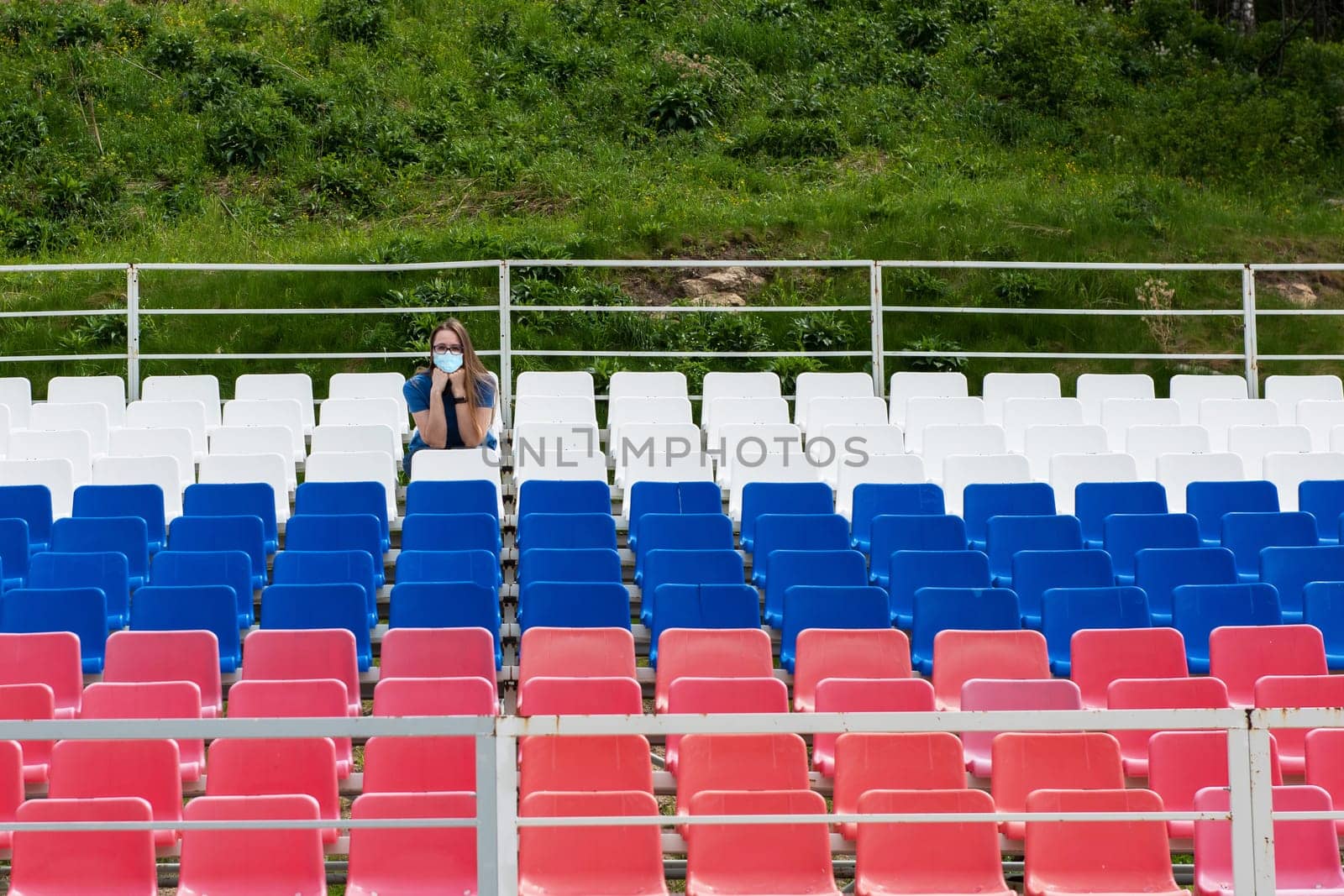 Lonely woman with protective mask on the empty stadium outdoor. Empty tribune due to pandemic Covid-19. Concept of pandemic life , empty stadiums, distance from viewers, safety.