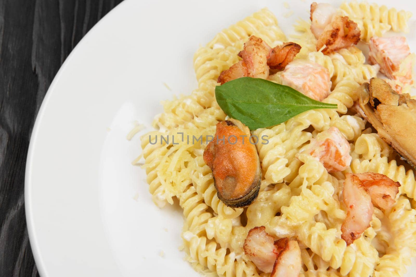 Seafood Pasta with mussels salmon and shrimps with basil in white plate on black wooden background.