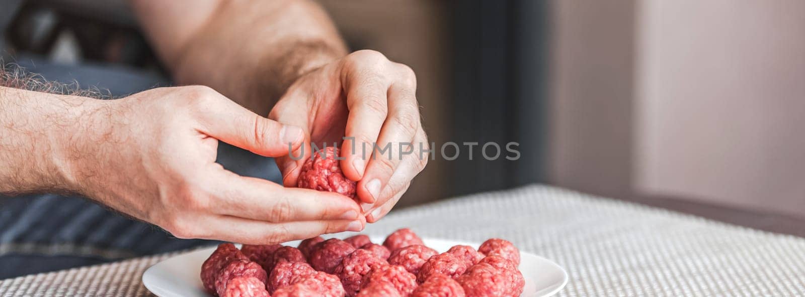 Man hands preparing meatballs with raw mincemeat. Lifestyle close up composition with natural light. Homemade cooking during lockdown, stay home housekeeping sharing concept. Side view with copy space