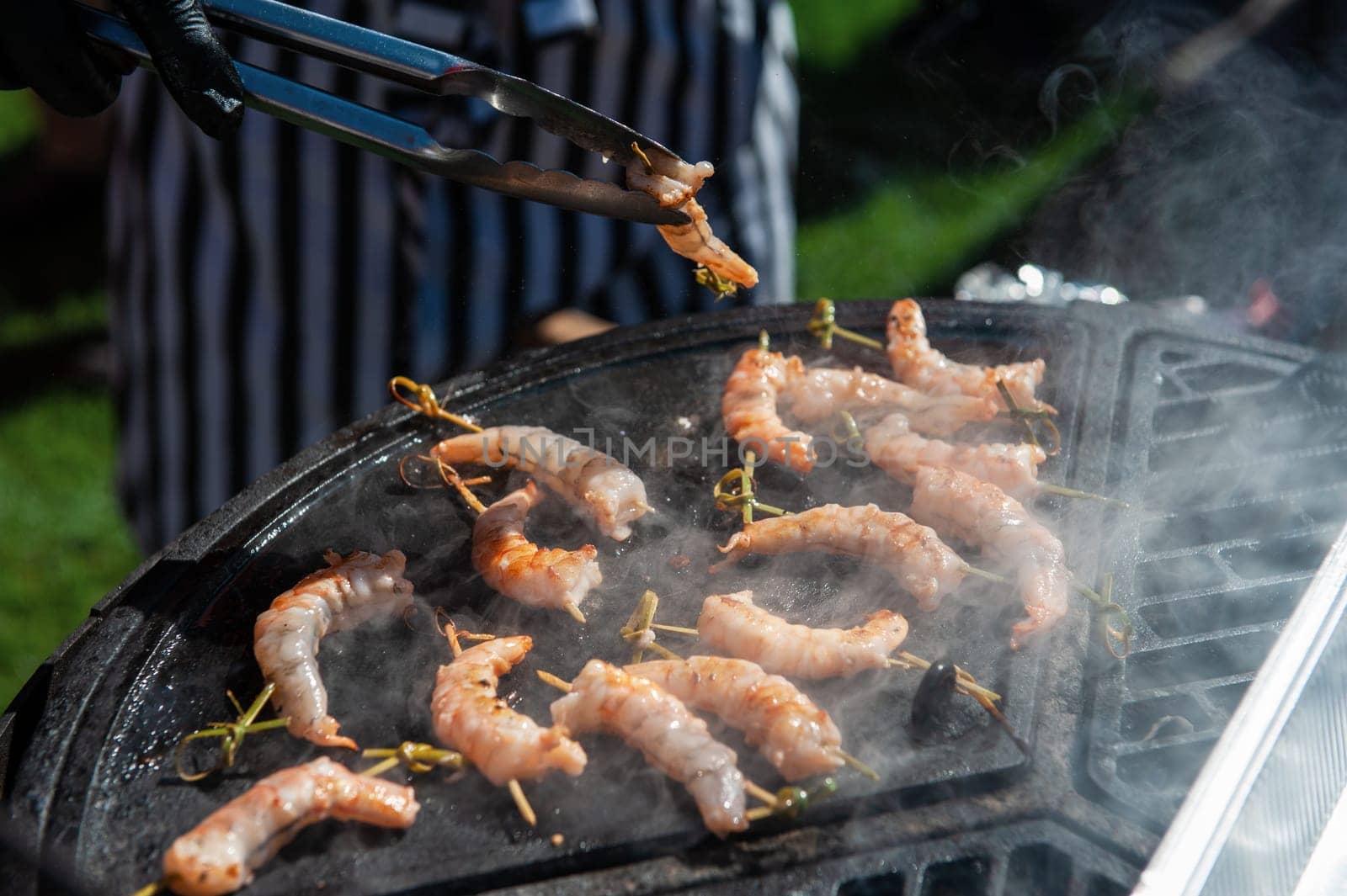 A professional cook prepares shrimps on the grill outdoor, food or catering concept