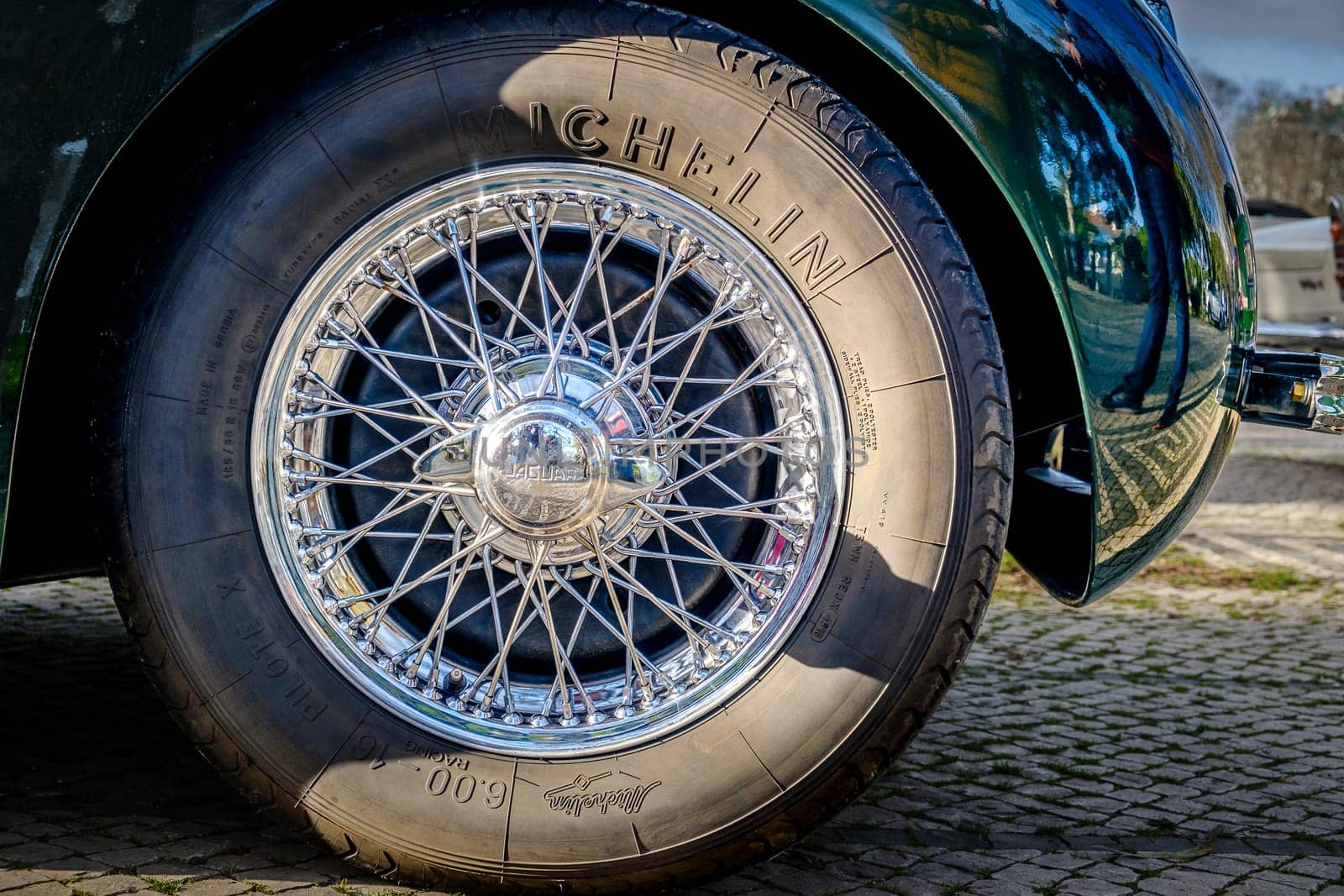 Lisbon, Portugal - Jan 20, 2024: Car design detail of Jaguar chrome wire wheel, stainless steel spokes, polished and chrome-plated with signs of wear-and-tear and bespoke 2-eared wire wheel spinner for splined hub with Jaguar logo. Michelin tyre.
