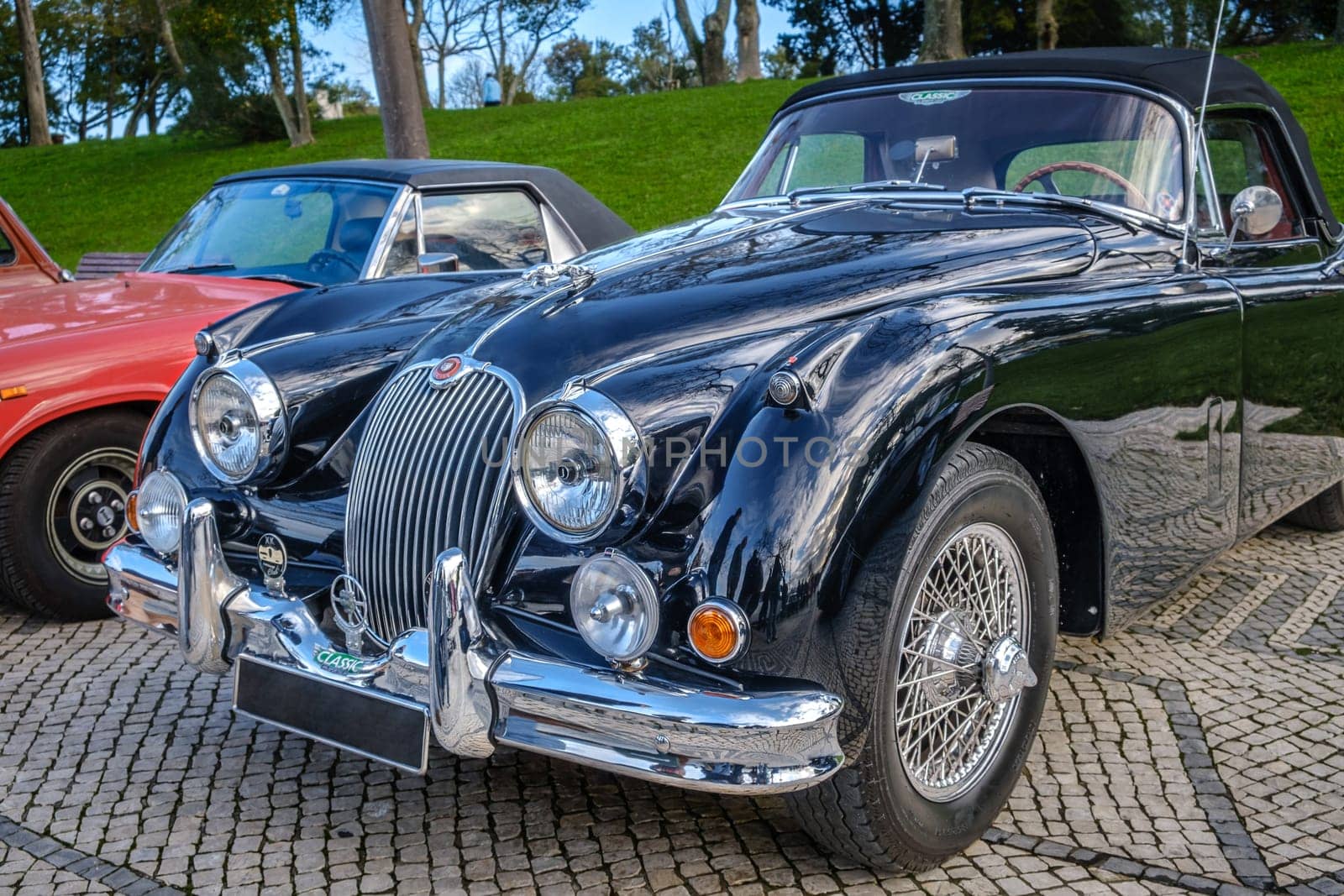 Lisbon, Portugal - Jan 20, 2024: Vintage dark green Jaguar XK150 drophead coupe car car parked on cobblestone pavement road. Two-seater roadster, sports car, convertible