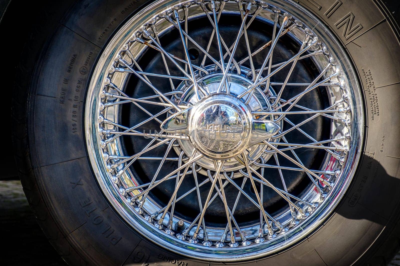 Lisbon, Portugal - Jan 20, 2024: Car design detail of Jaguar chrome wire wheel, stainless steel spokes, polished and chrome-plated with signs of wear-and-tear and bespoke 2-eared wire wheel spinner for splined hub with Jaguar logo. Michelin tyre.