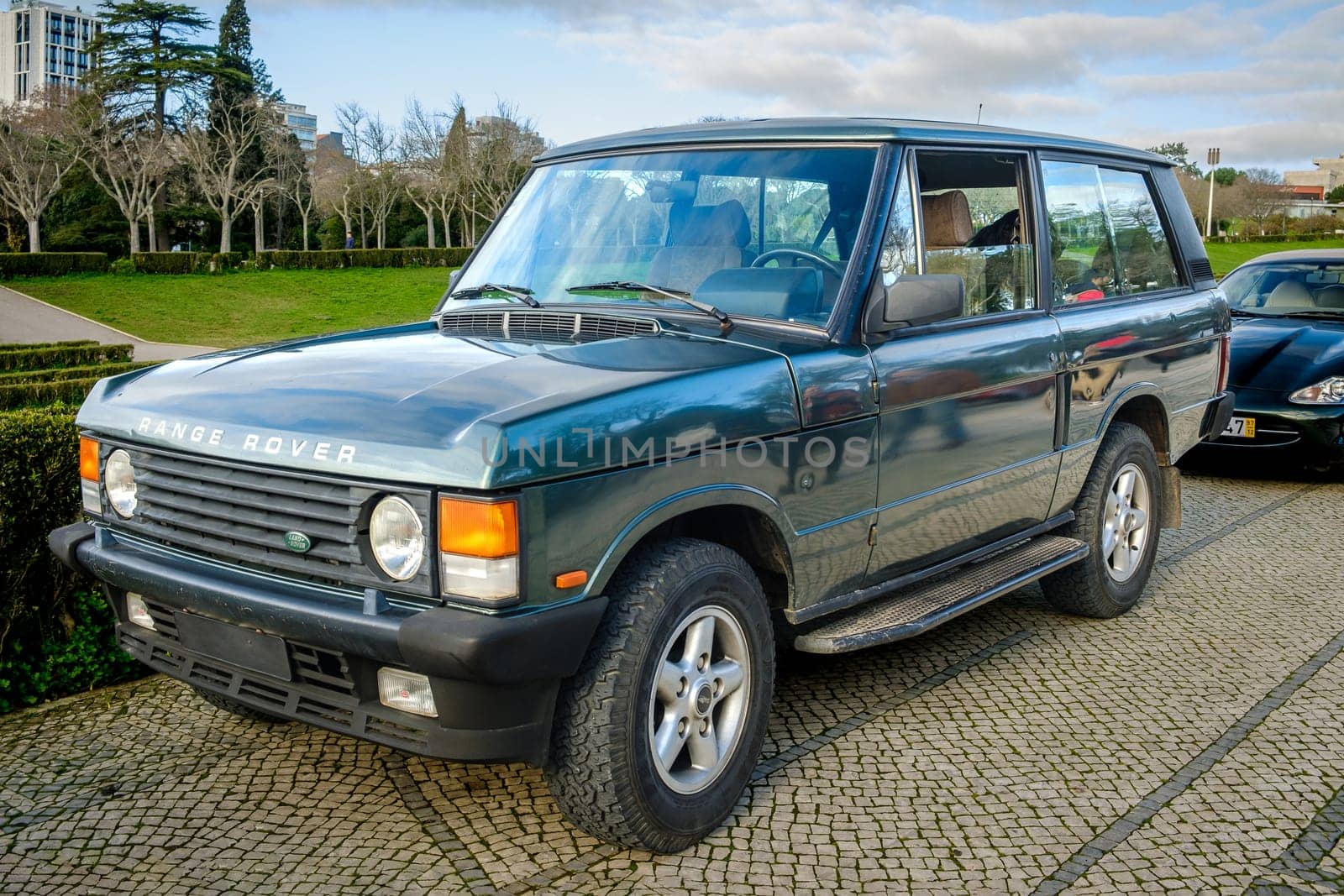 Lisbon, Portugal - Jan 20, 2024: A classic green Land Rover Range Rover car parked on a cobblestone path near green park. 4x4, mid-size off-road vehicle as two-door model of first generation.