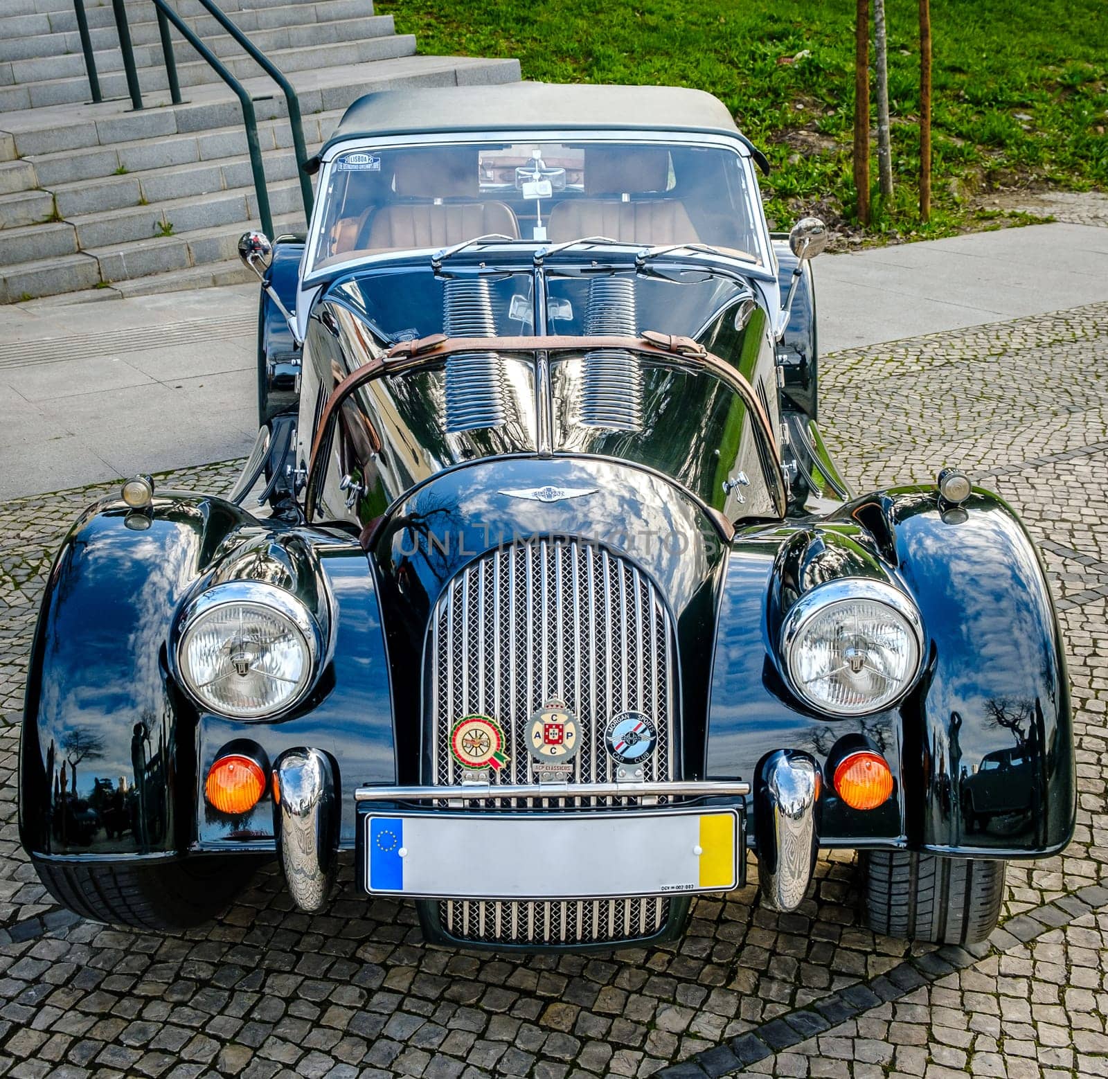 Lisbon, Portugal - Jan 20, 2024: A classic dark green Morgan Plus 4 sports car with chrome detailing parked on a cobblestone path near green park.