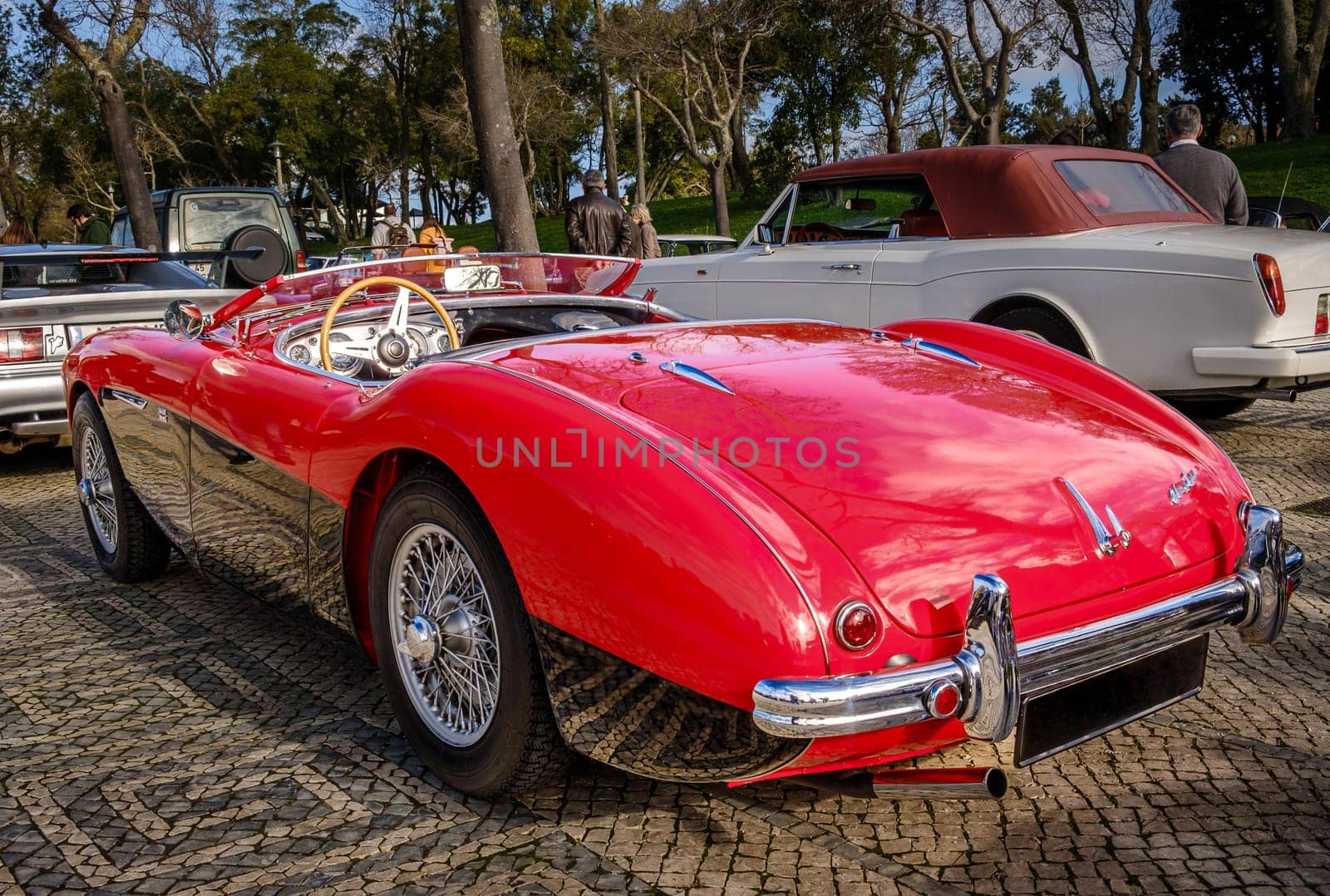 Lisbon, Portugal - Jan 20, 2024: Rear view of two-tone Reno red and black Austin-Healey 100 vintage convertible sports car parked on cobblestone pavement road. Red velvet and leather, wooden steering wheel, fold-down windshield