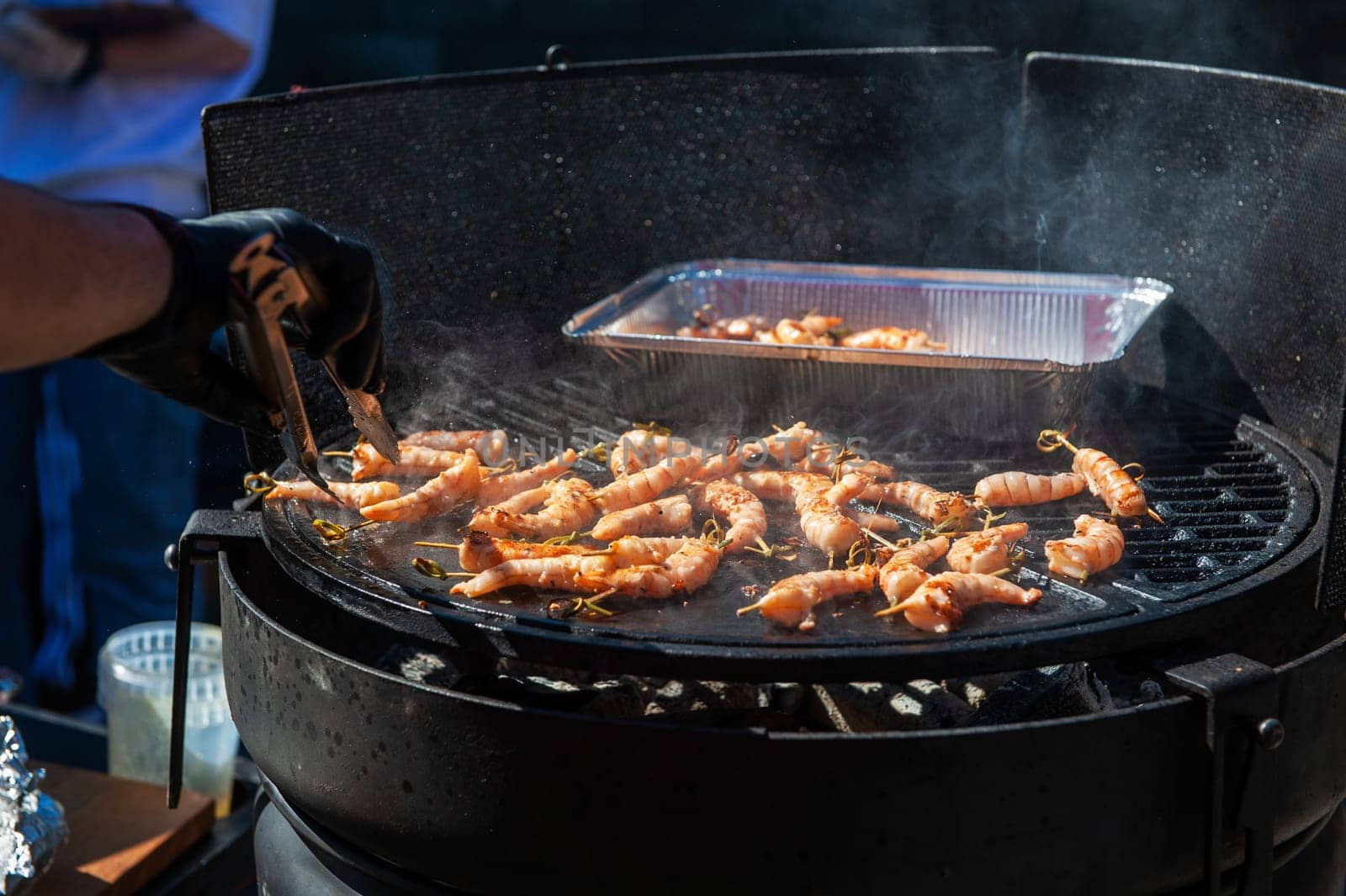 A professional cook prepares shrimps on the grill outdoor, food or catering concept