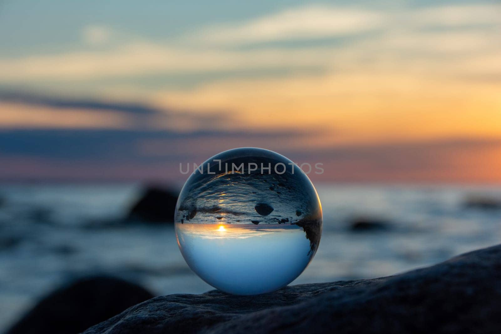 Glass ball on a rock at sunset on the beach, the sea and the setting sun are reflected in the ball