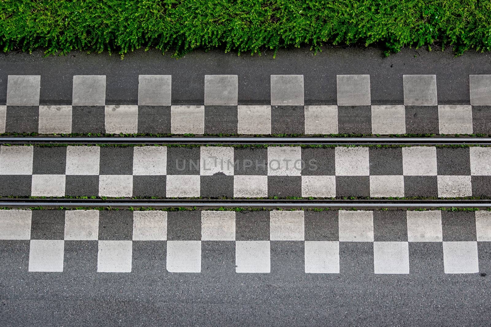 Directly above view of tram tracks running between rows of checkered tiles, bordered by greens