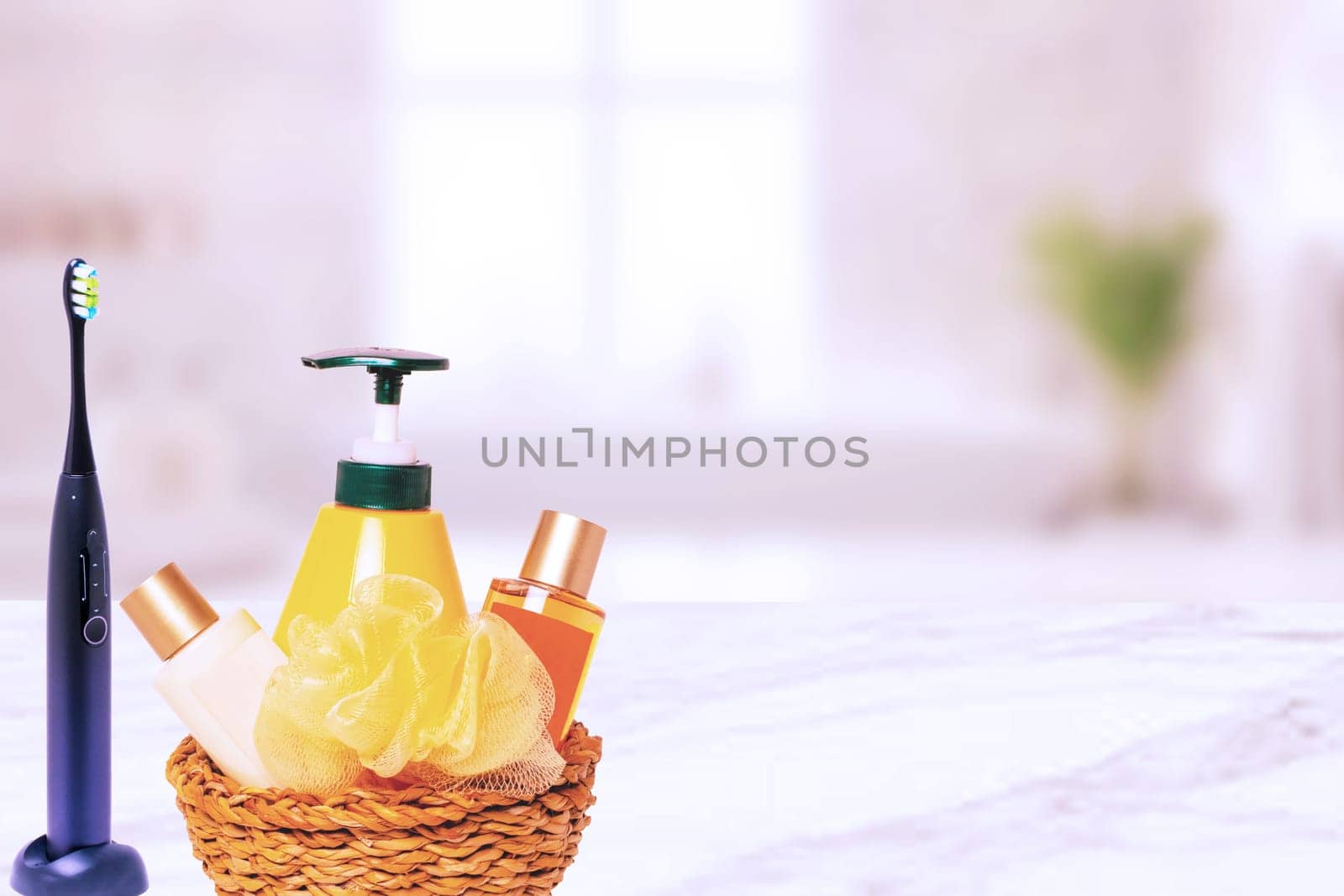 A straw basket with cosmetics and soap dispender and a electrical tooth brush over abstract blurred bath background. Bath products and skincare. Spa treatment. Hotel accessories.