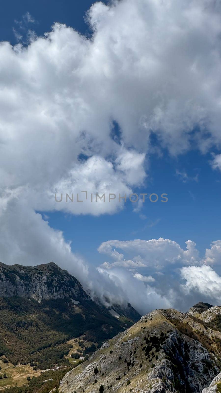 A dramatic scene of rugged mountain peaks partially covered by dense clouds, with clear blue sky peeking through.