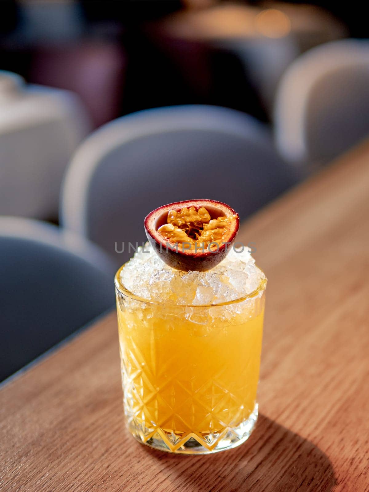 Yellow old-fashioned refreshing cocktail with whiskey and crushed ice on bar counter. Vertical. Alcohol or non-alcohol cold cocktail decorated passion fruit. Copy space.