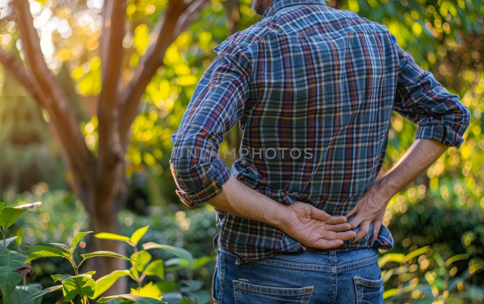 An individual outdoors clutching their lower back in pain. The natural setting contrasts with the uncomfortable subject of back pain