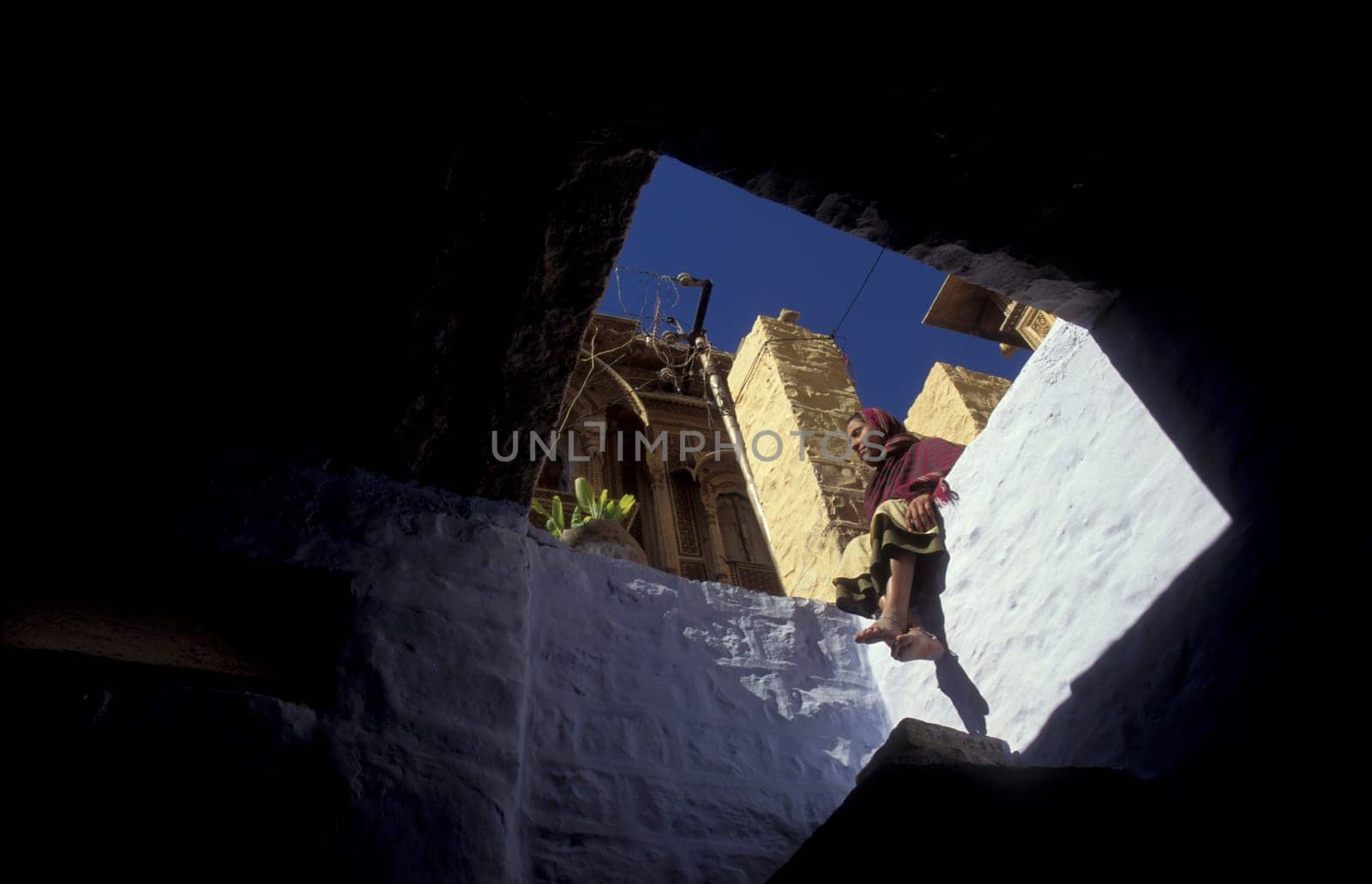 a women sits on her balcony in the old Town in the Jaisalmer Fort with the city of Jaisalmer in the Province of Rajasthan in India.  India, Jaisalmer, January, 1998