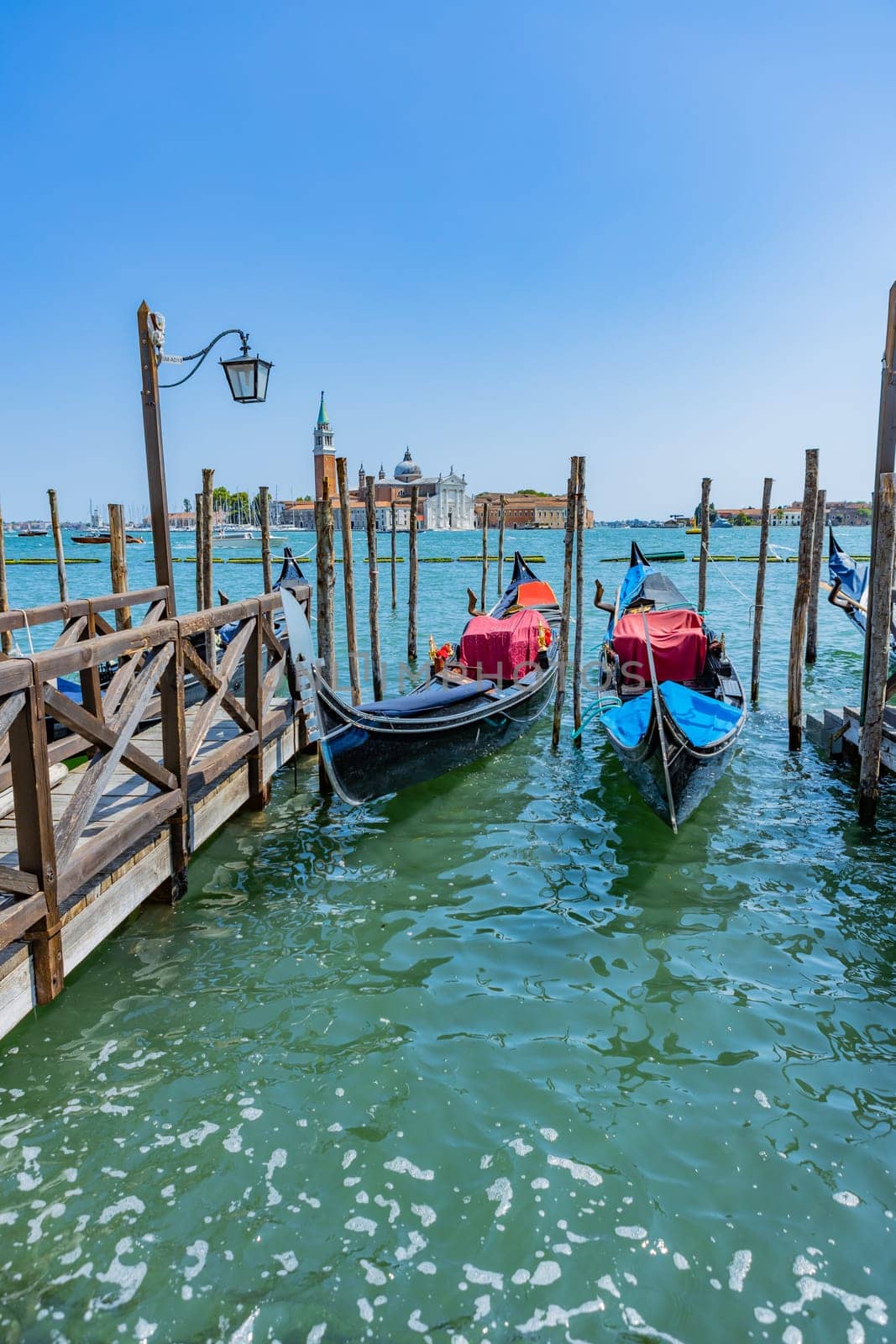 Venice, Italy - July 26, 2024: Gondolas against the San Giorgio island in Venice, Italy. Gondola is the most attractive tourist transport in Venice. Traveling and vacation in sunny Venice.