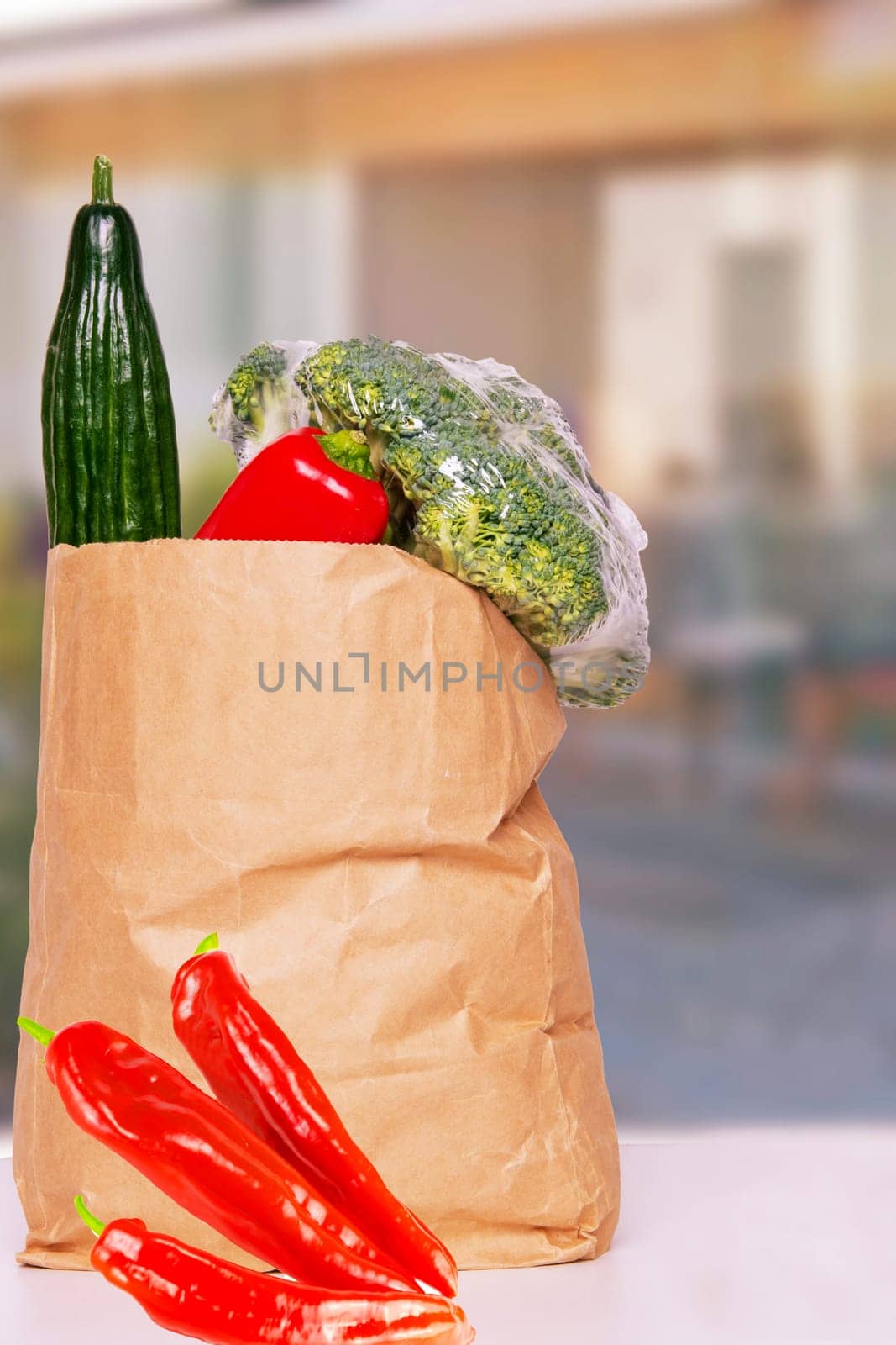 Closeup of a brown paper shopping bag with fresh vegetables and paprika on table over abstract blurred house background. Space. Concept of strengthening the immune system.