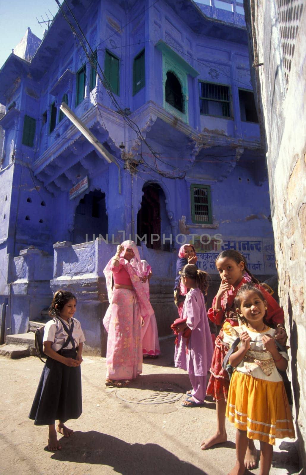 people in front of a blue painted living House in the Blue City and Town of Jodhpur in the Province of Rajasthan in India.  India, Jodhpur, January, 1998