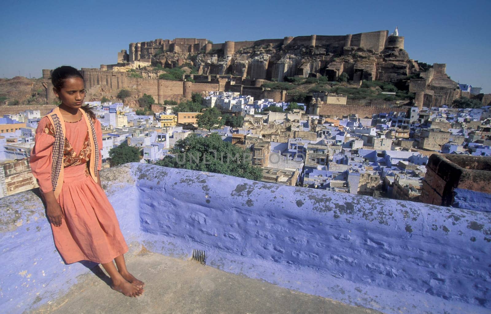 a Women on her Roof Top a view of the Meherangarh in the Town and Blue City of Jodhpur in the Province of Rajasthan in India.  India, Jodhpur, January, 1998