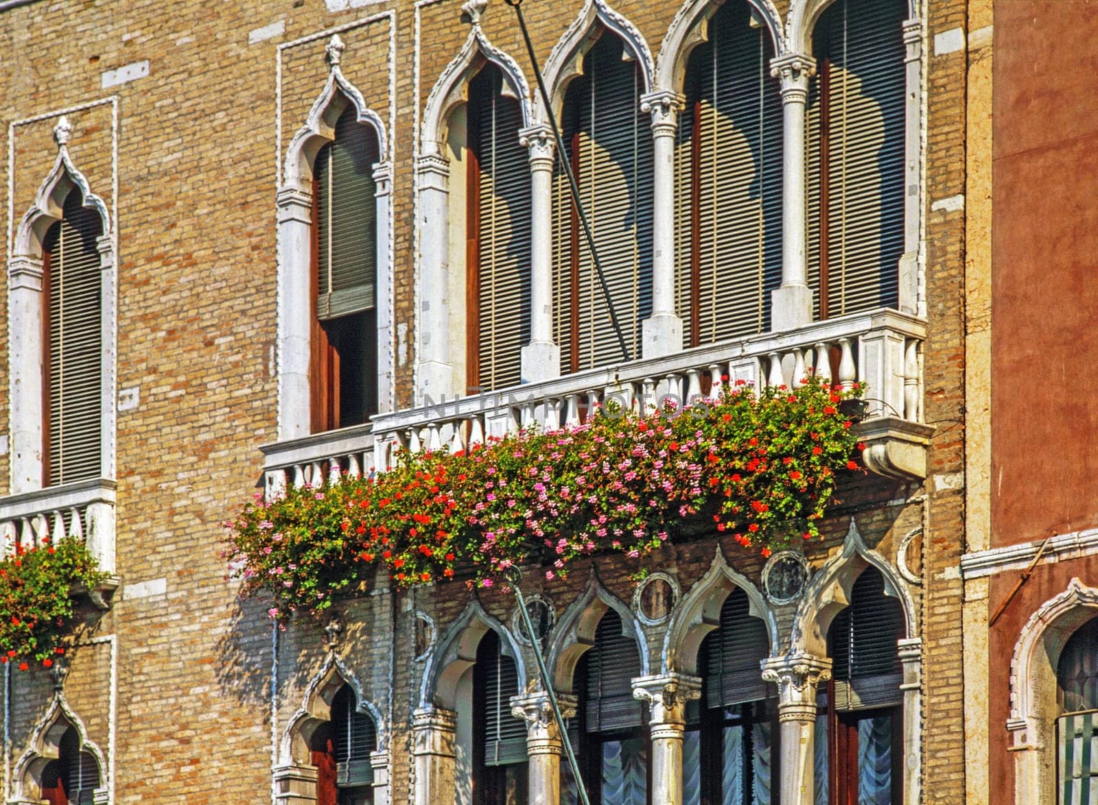 Windows with shades and balcony with flowers on Venice palace, Italy