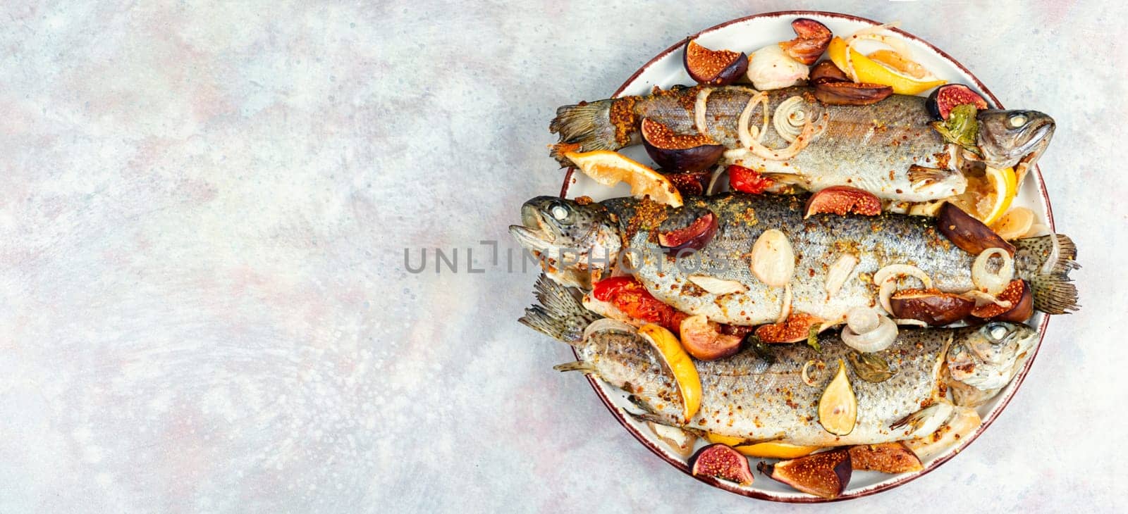 Baked whole river trout with ripe figs on a concrete kitchen table. Flat lay