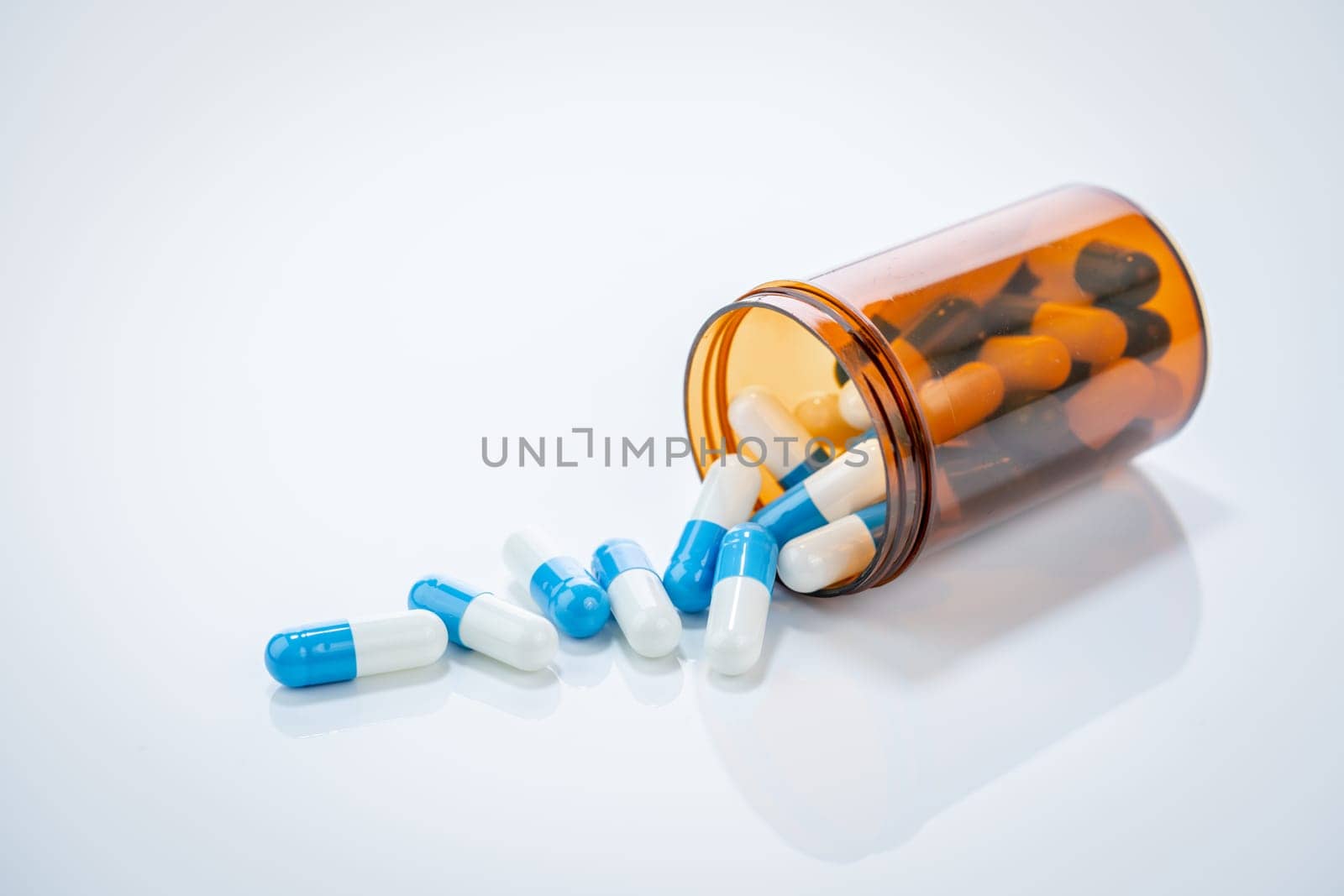 Prescription antibiotic capsules spilling from amber bottle on white background. Blue and white capsule pills. Healthcare and pharmaceutical. Medical treatment pills. Pharmacy and medicine industry.