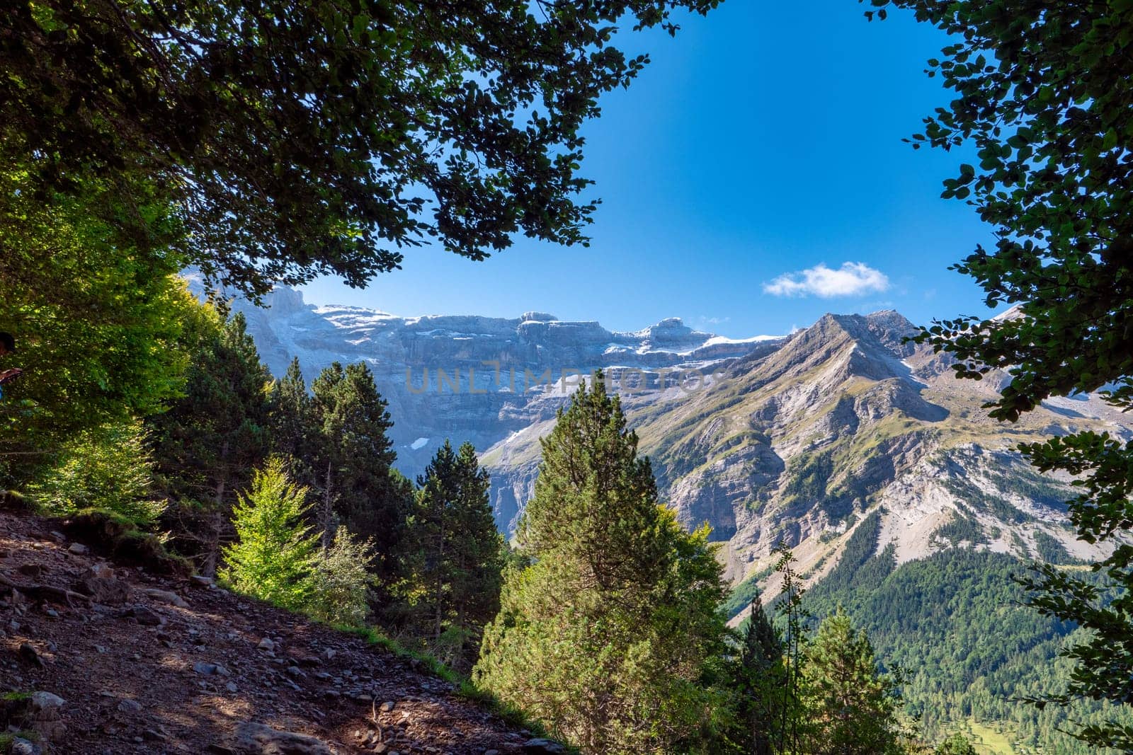 The Cirque of Gavarnie, french Pyrenes mountains. The mountains are covered in snow and the sky is cloudy. The river is surrounded by a lush green valley