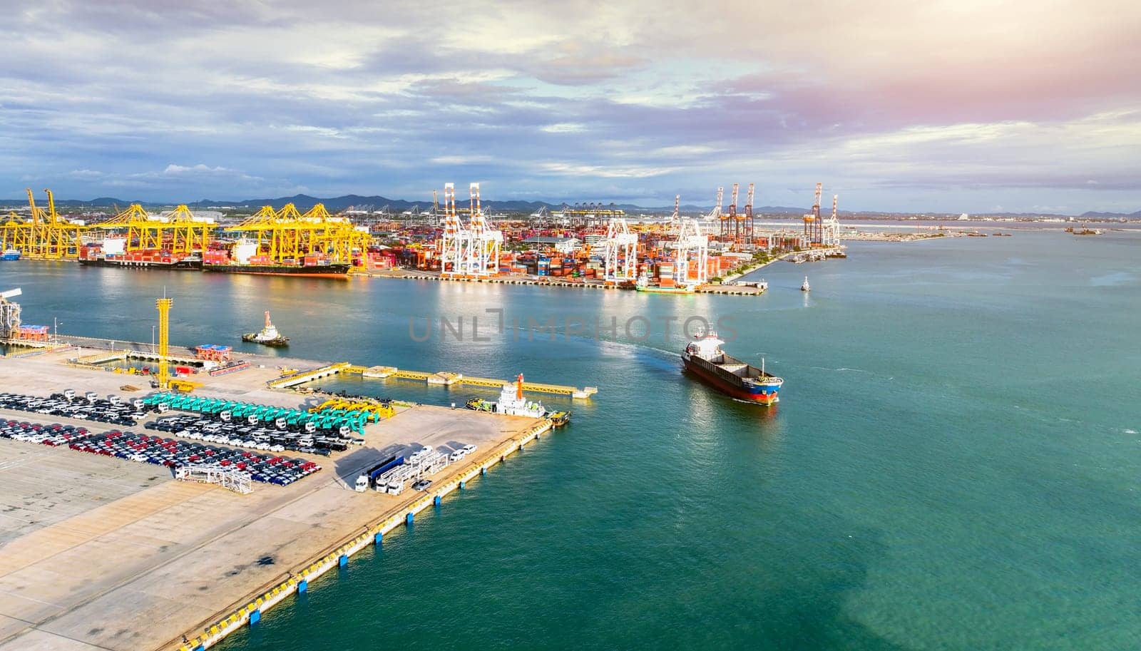 Aerial view of a large stock of new cars parked at a port terminal. Automotive industry logistics and transport operations. Import and export of vehicles by ship, with containers ready global trade.