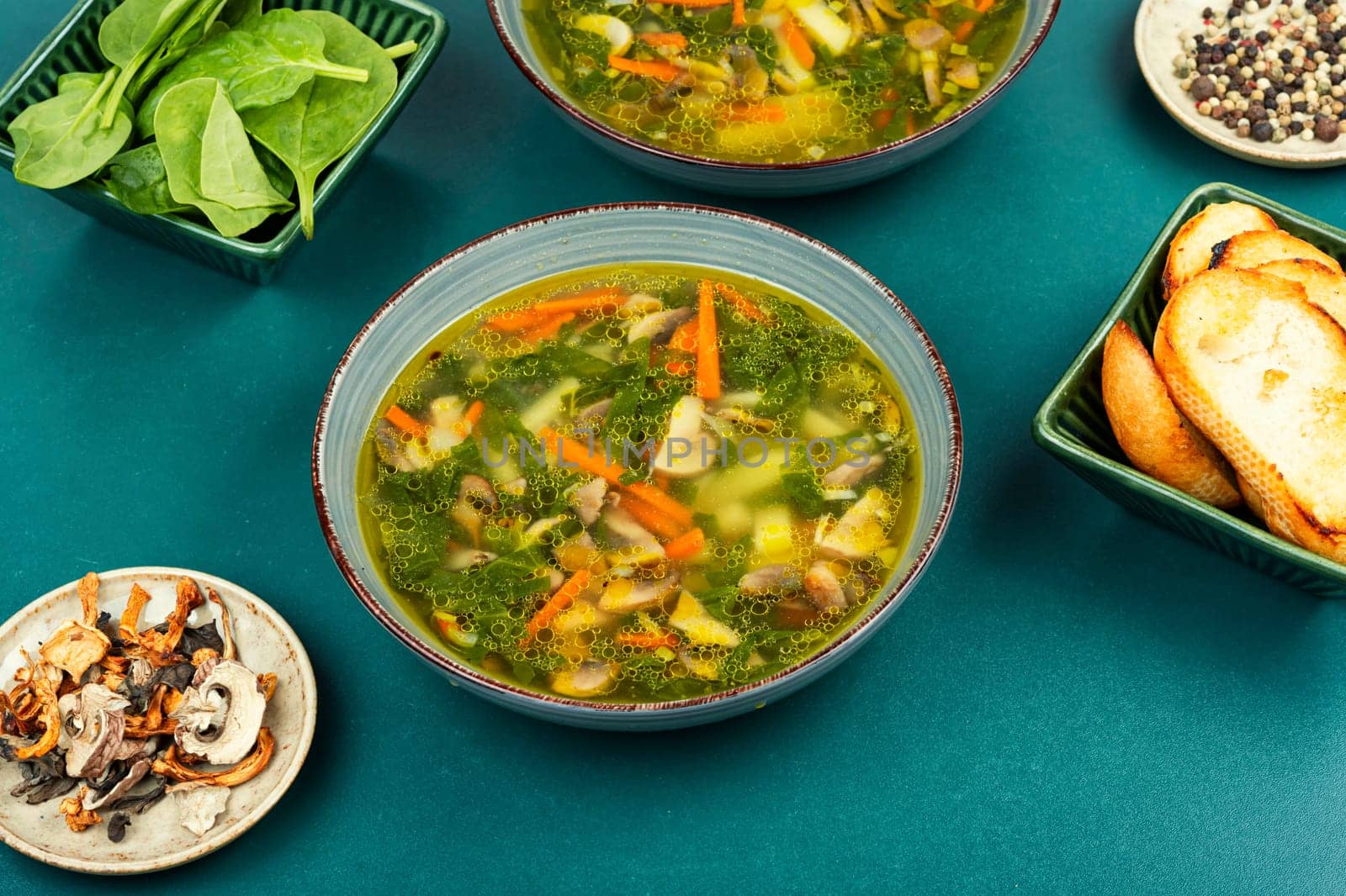Homemade thick vegetarian mushroom soup with spinach and vegetables on rustic wooden table.